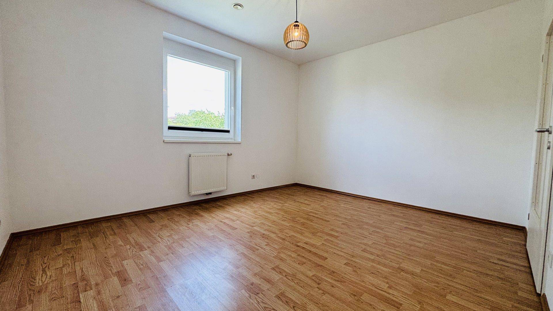 Helles Schlafzimmer mit Laminatboden, weißen Wänden und einem großen Fenster.