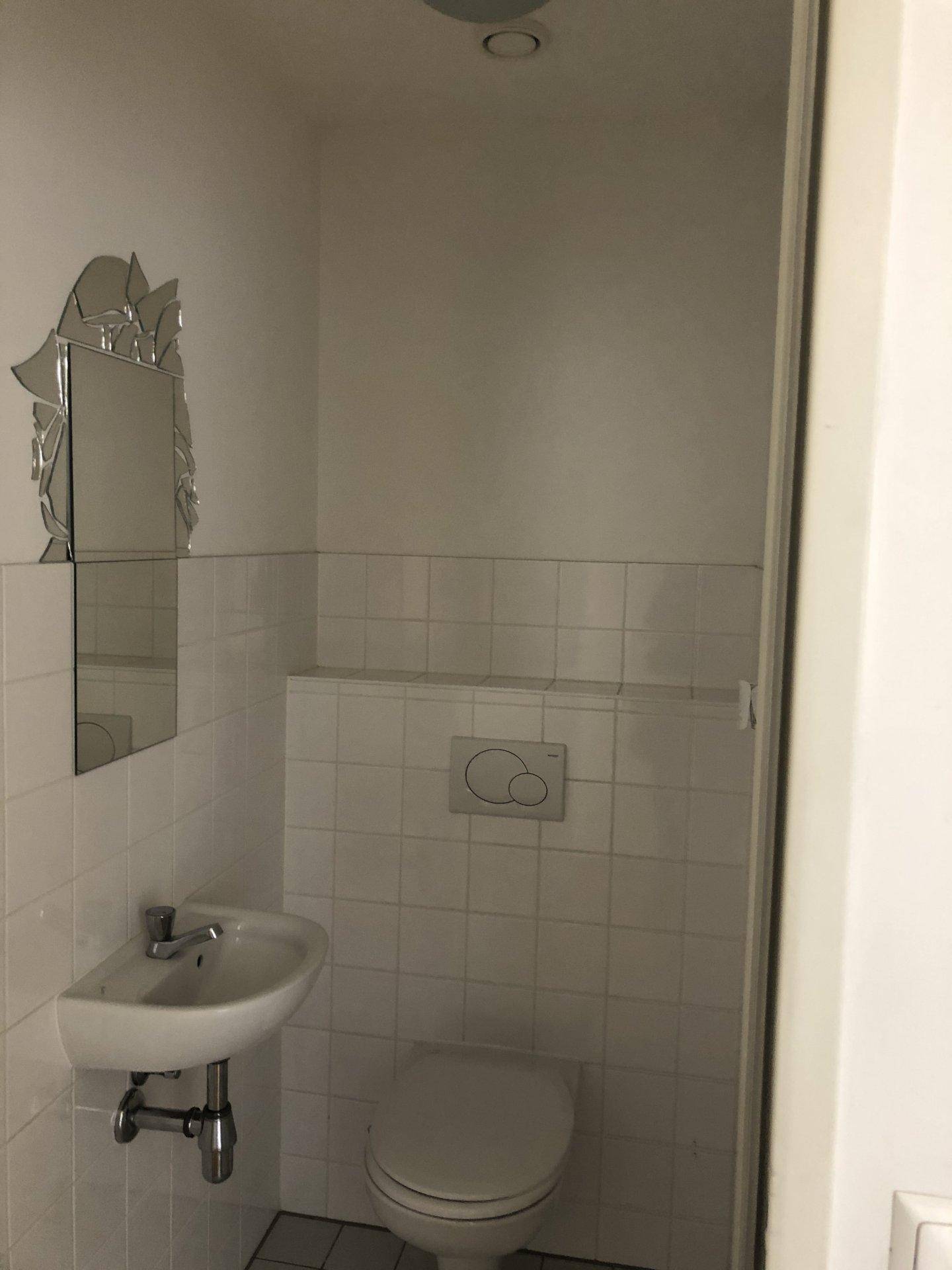 Kleines Gäste-WC mit weißen Fliesen, Waschbecken und Wandspiegel.
