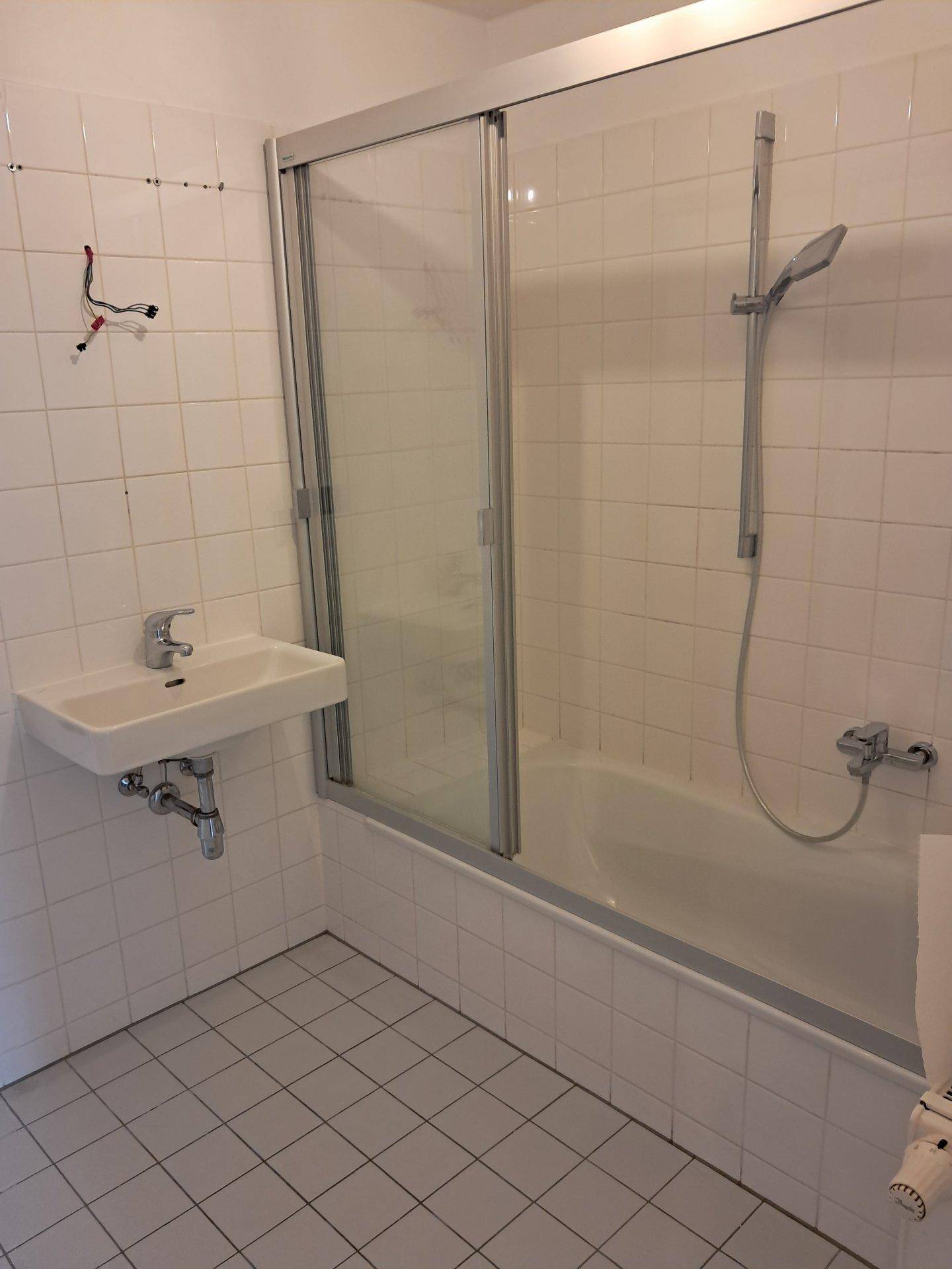 Badezimmer mit Badewanne, Duschvorrichtung und Waschbecken, komplett gefliest.