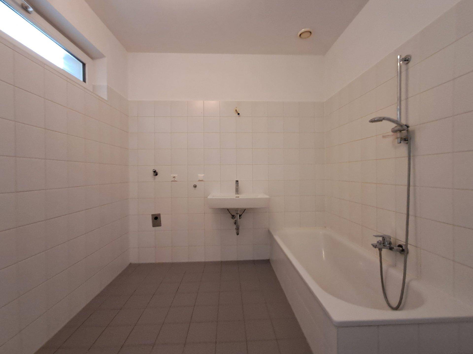 Modernes Badezimmer mit weißen Fliesen, Badewanne, kleinem Waschbecken und Oberlichtfenster.