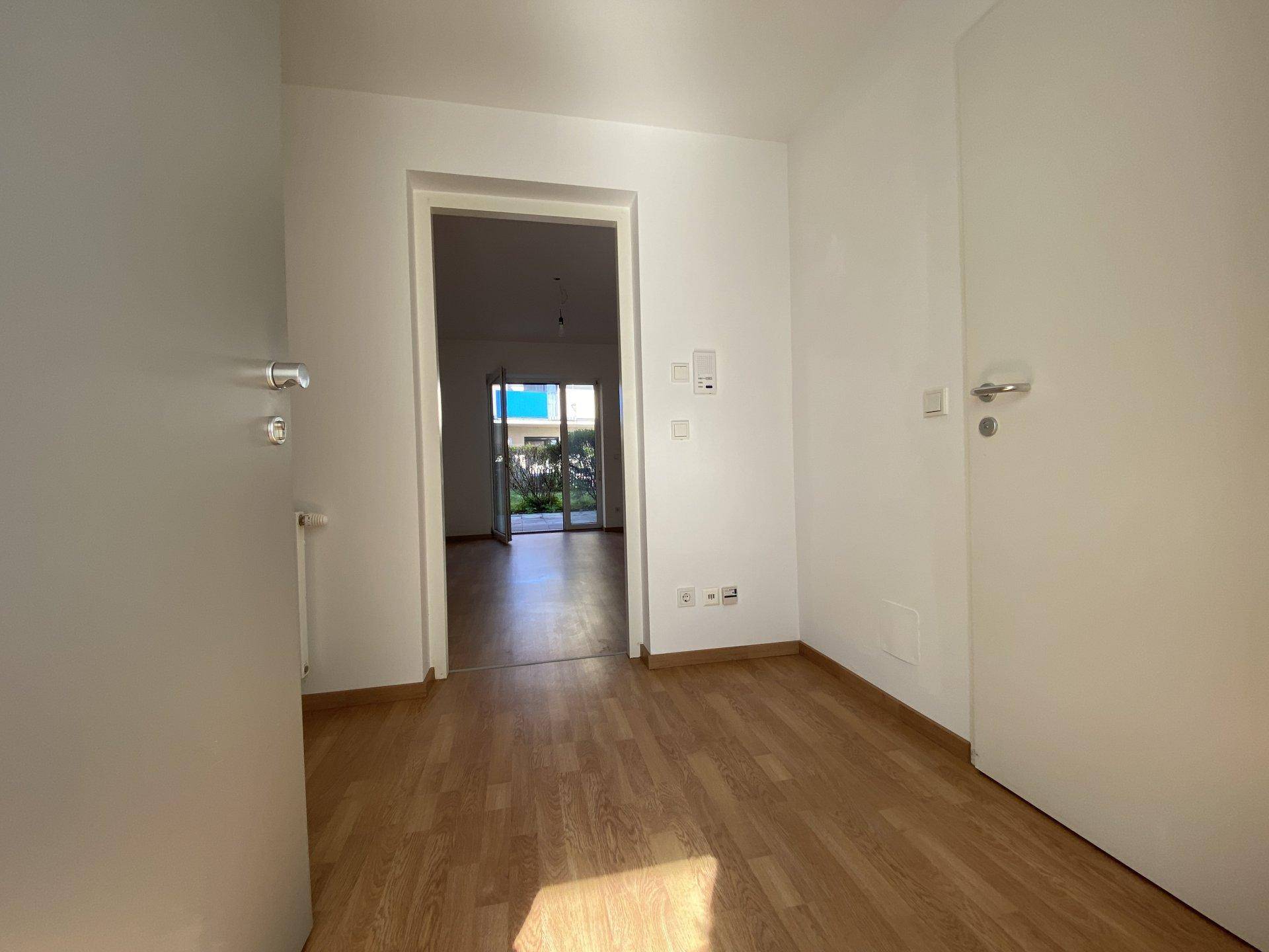Heller Flur mit Laminatboden und weiß gestrichenen Wänden, der in den Wohnbereich führt.