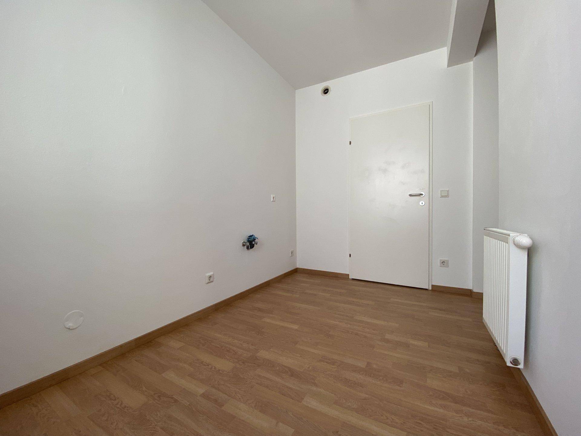 Unmöbliertes Zimmer mit Laminatboden, weiß gestrichenen Wänden und Heizkörper.