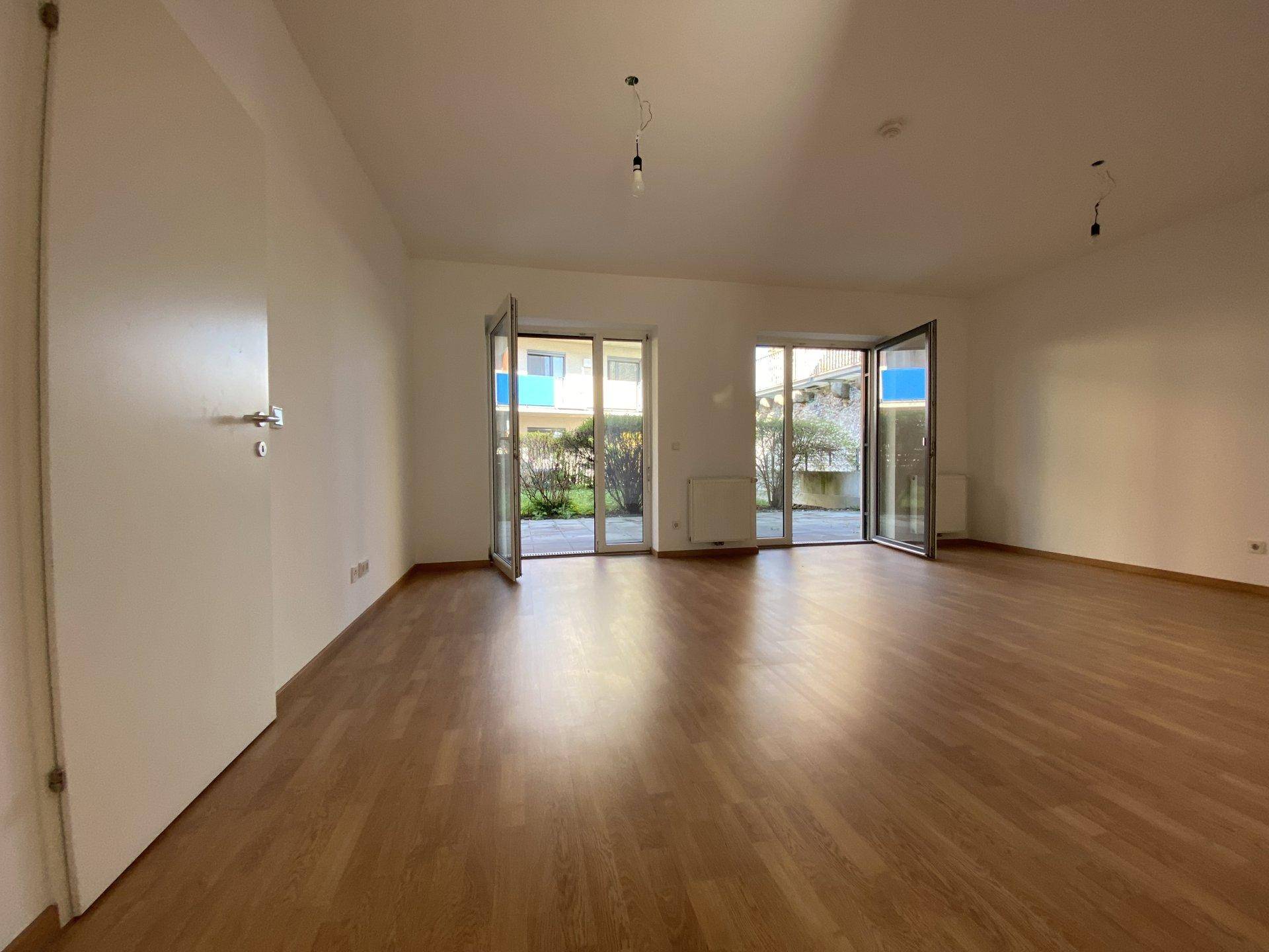 Geräumiges Wohnzimmer mit Laminatboden und zwei großen Türen, die zum Außenbereich führen.