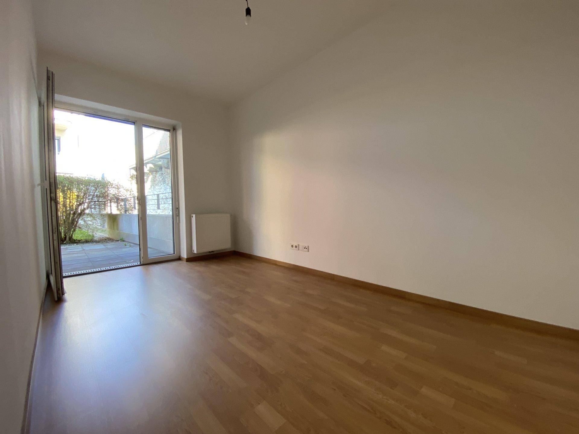 Leeres Zimmer mit Laminatboden und einer großen Schiebetür, die auf eine Terrasse führt.