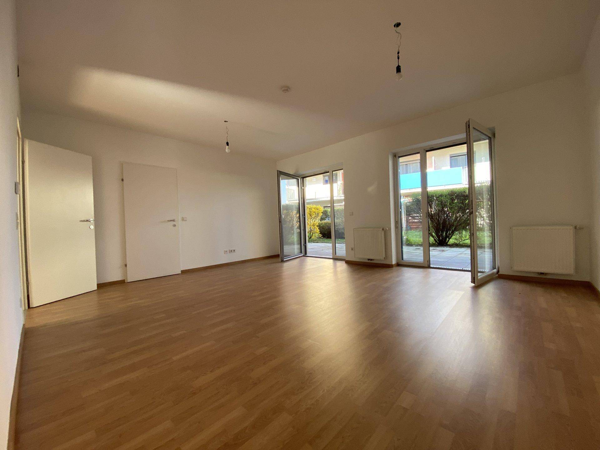 Helles Wohnzimmer mit Laminatboden und Zugang zu einer Terrasse, ideal für sonnige Tage.