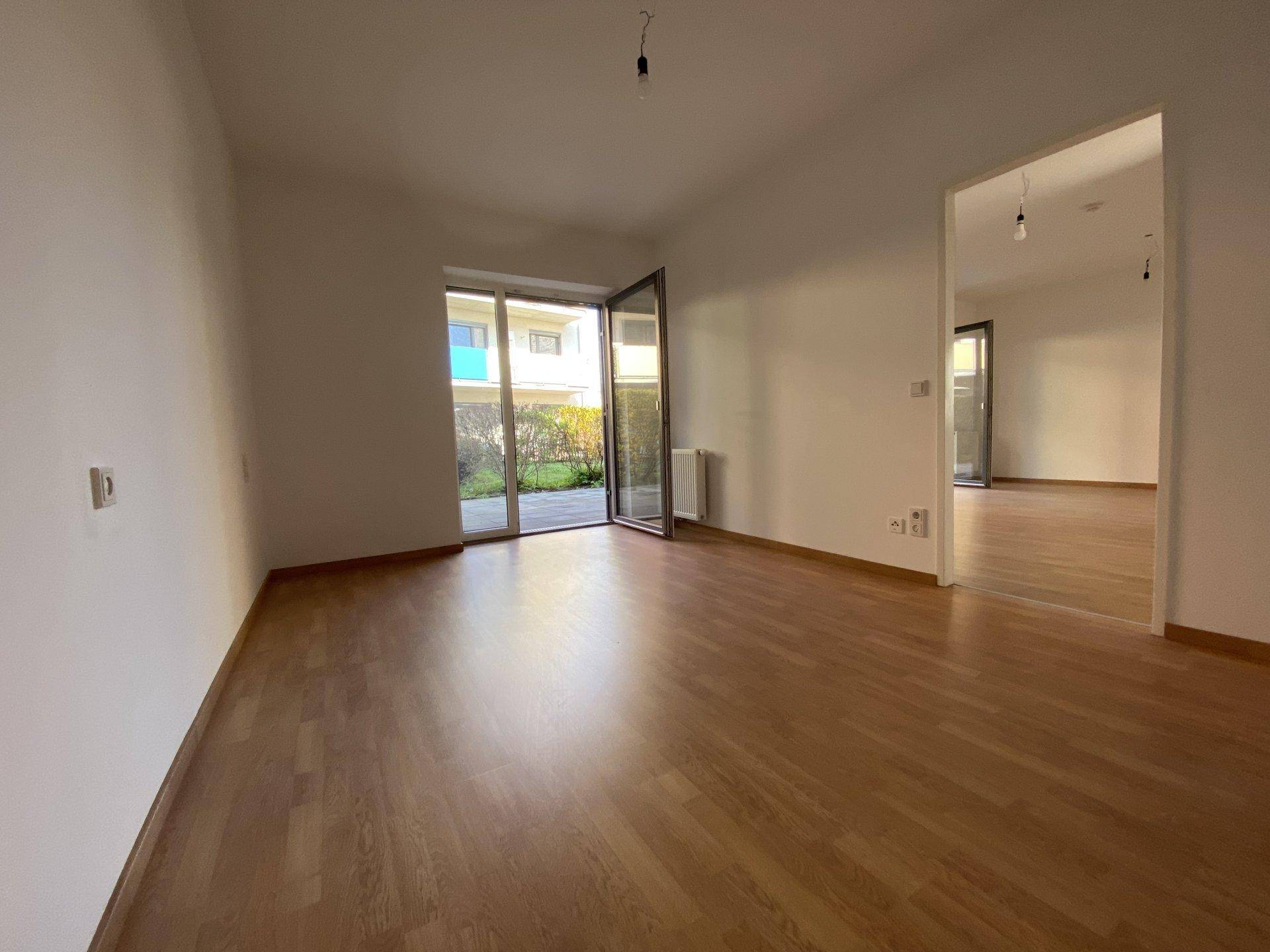 Heller Raum mit Laminatboden und Terrassenzugang, der offen zu einem weiteren Bereich führt.