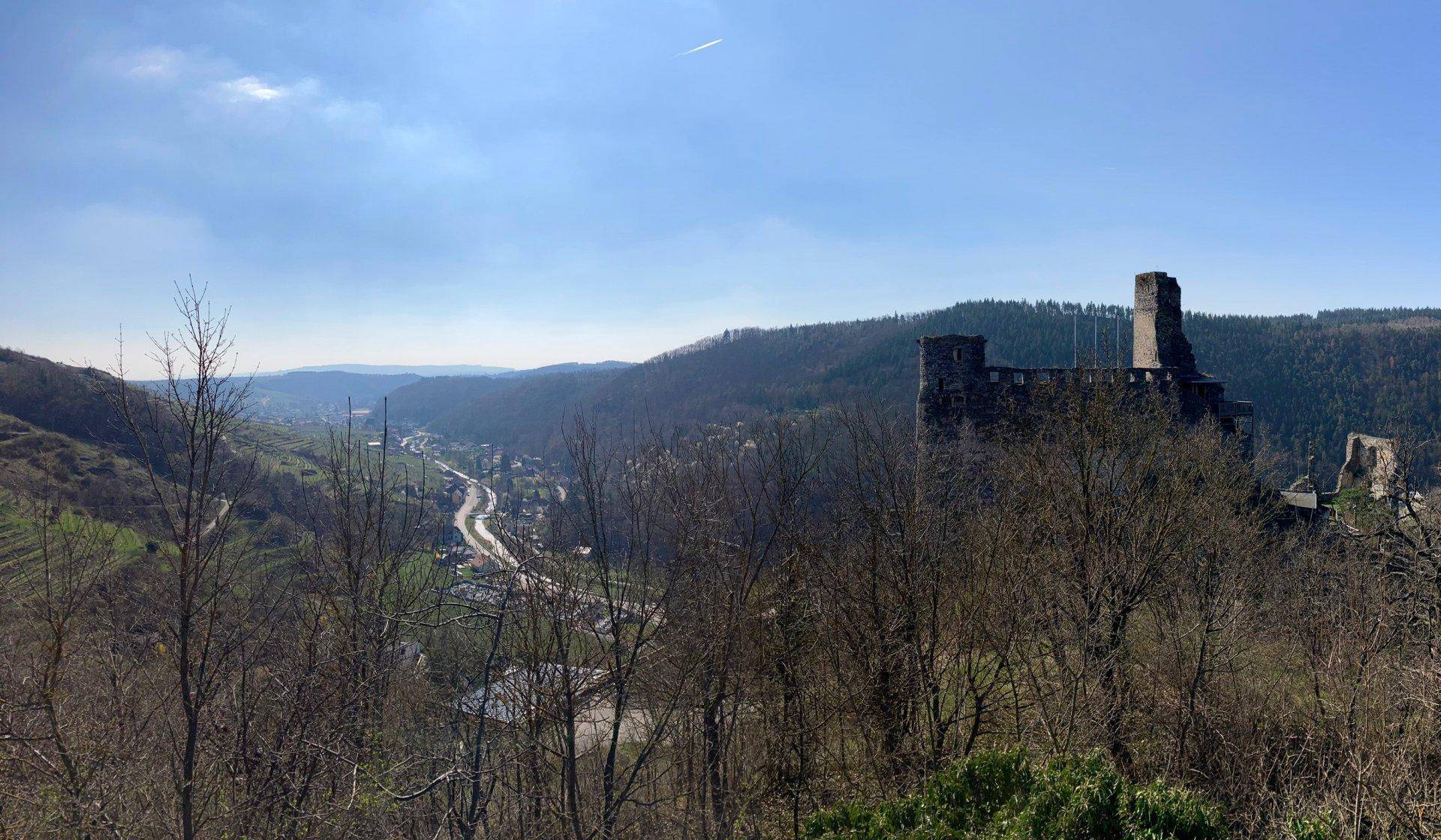 Malerischer Ausblick auf eine Burgruine auf einem Hügel und ein Tal mit einer Straße.