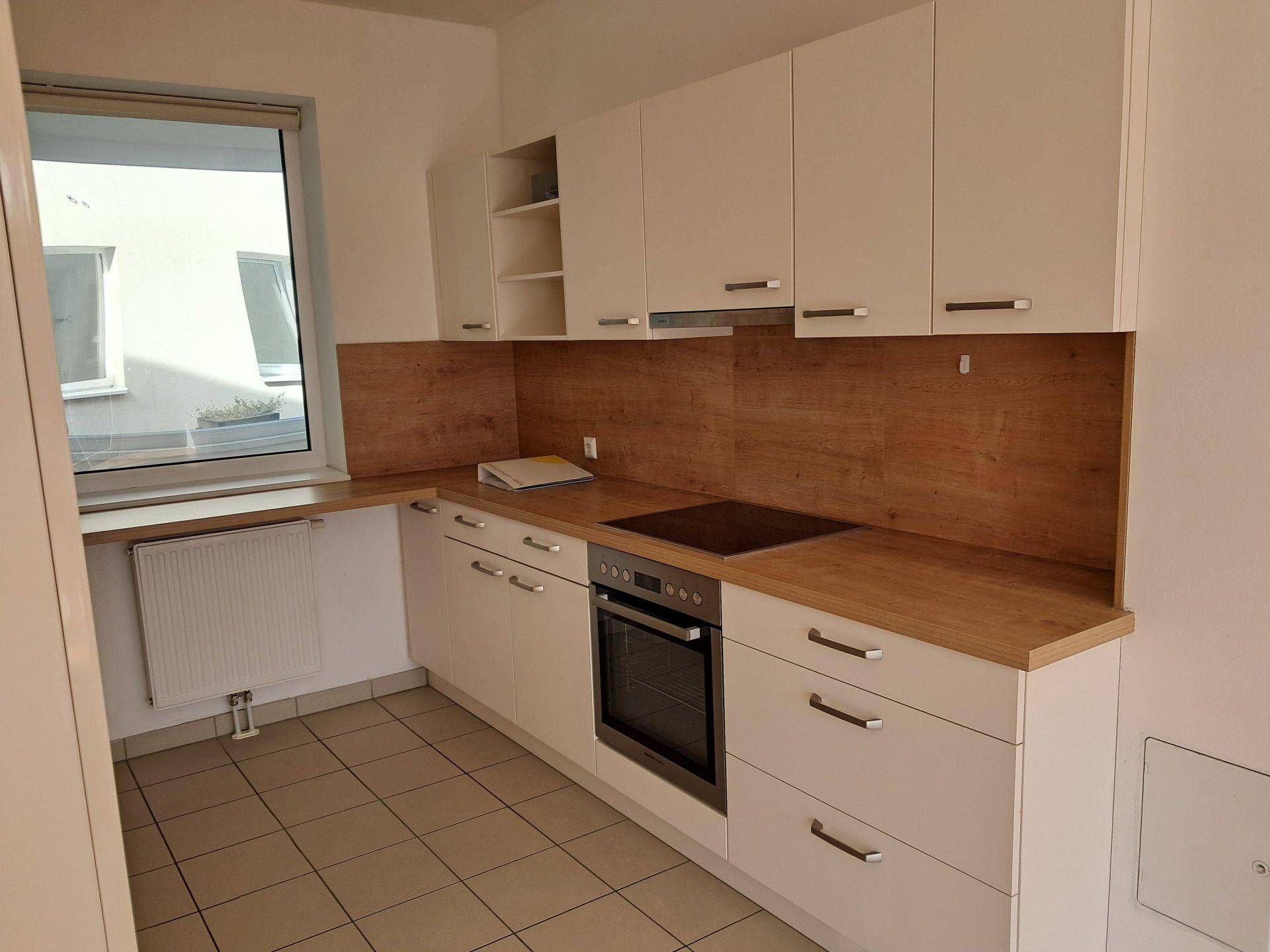 Moderne Küche mit weißen Schränken, Holzoptik-Arbeitsplatten und integriertem Kochfeld.