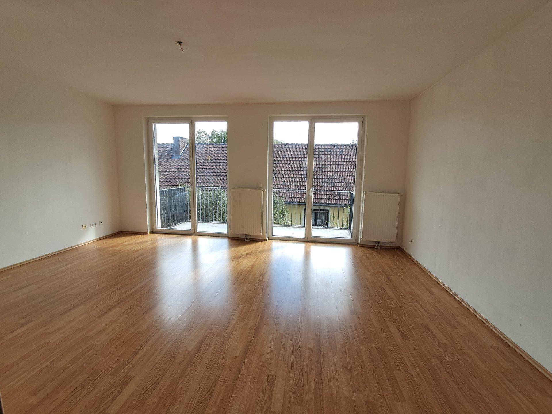 Leeres Wohnzimmer mit Laminatboden und Zugang zu einem Balkon.