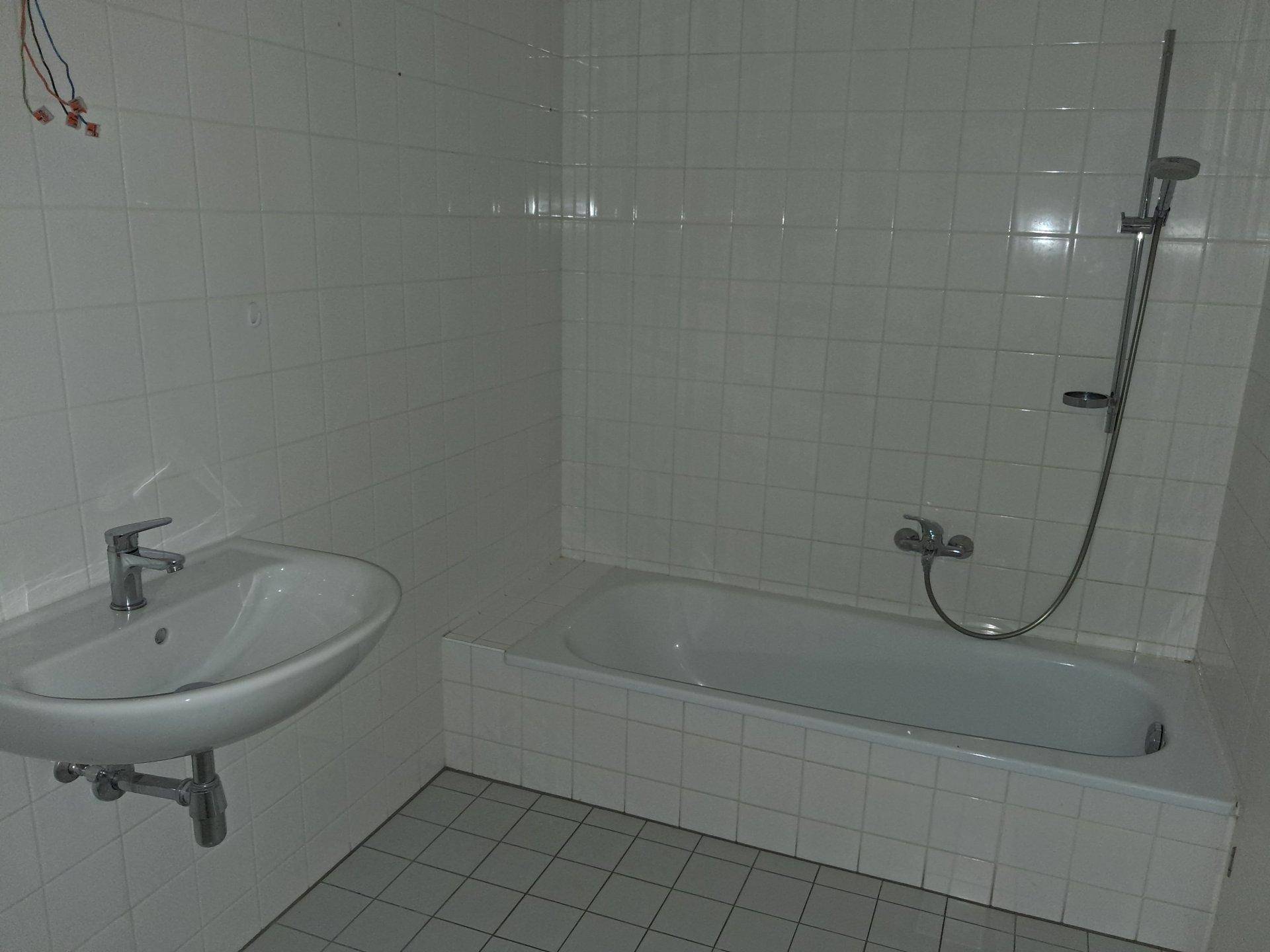 Einfaches Badezimmer mit Badewanne, Waschbecken und weißen Fliesen.