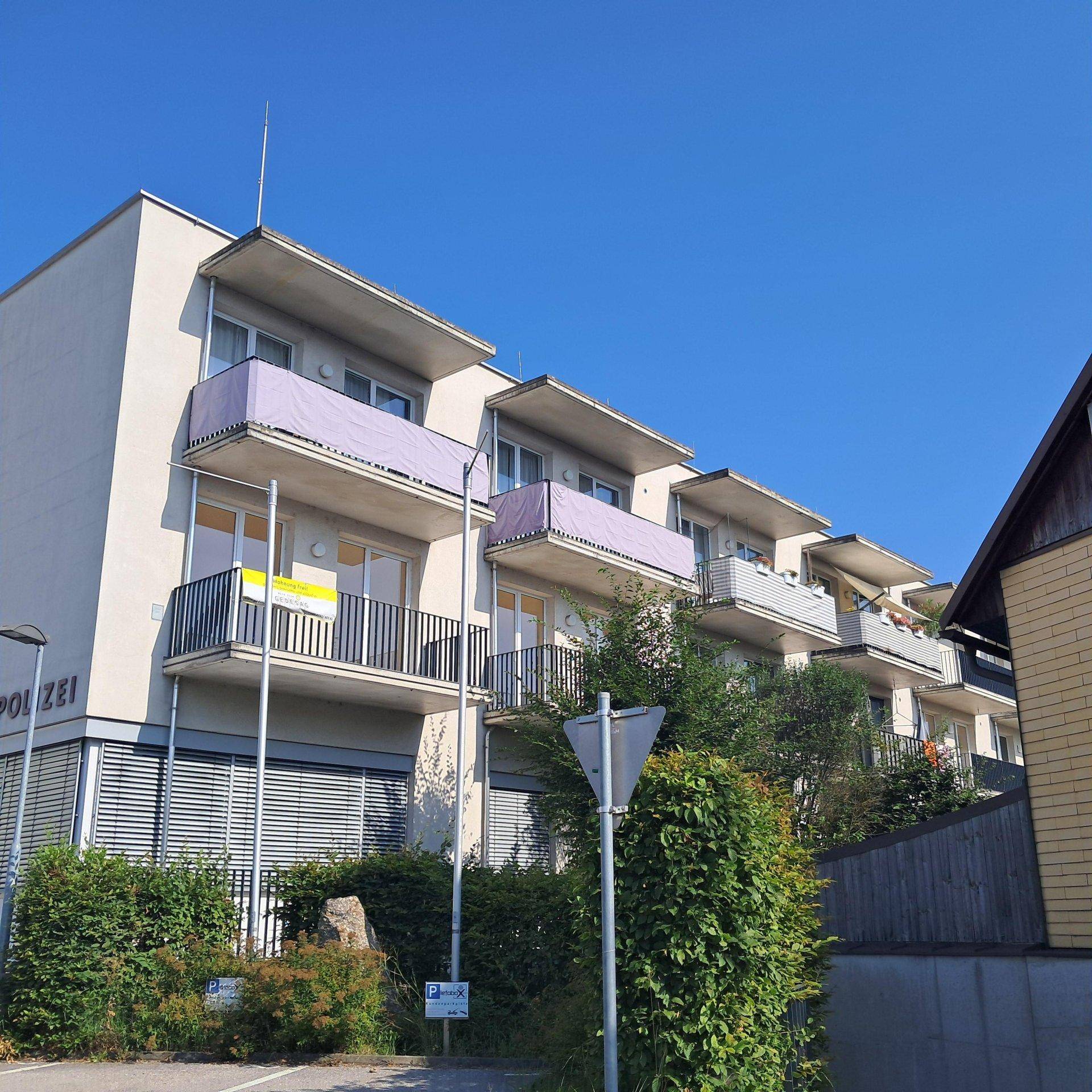 Seitenansicht des Mehrfamilienhauses mit Balkonen und grüner Bepflanzung im Vordergrund.