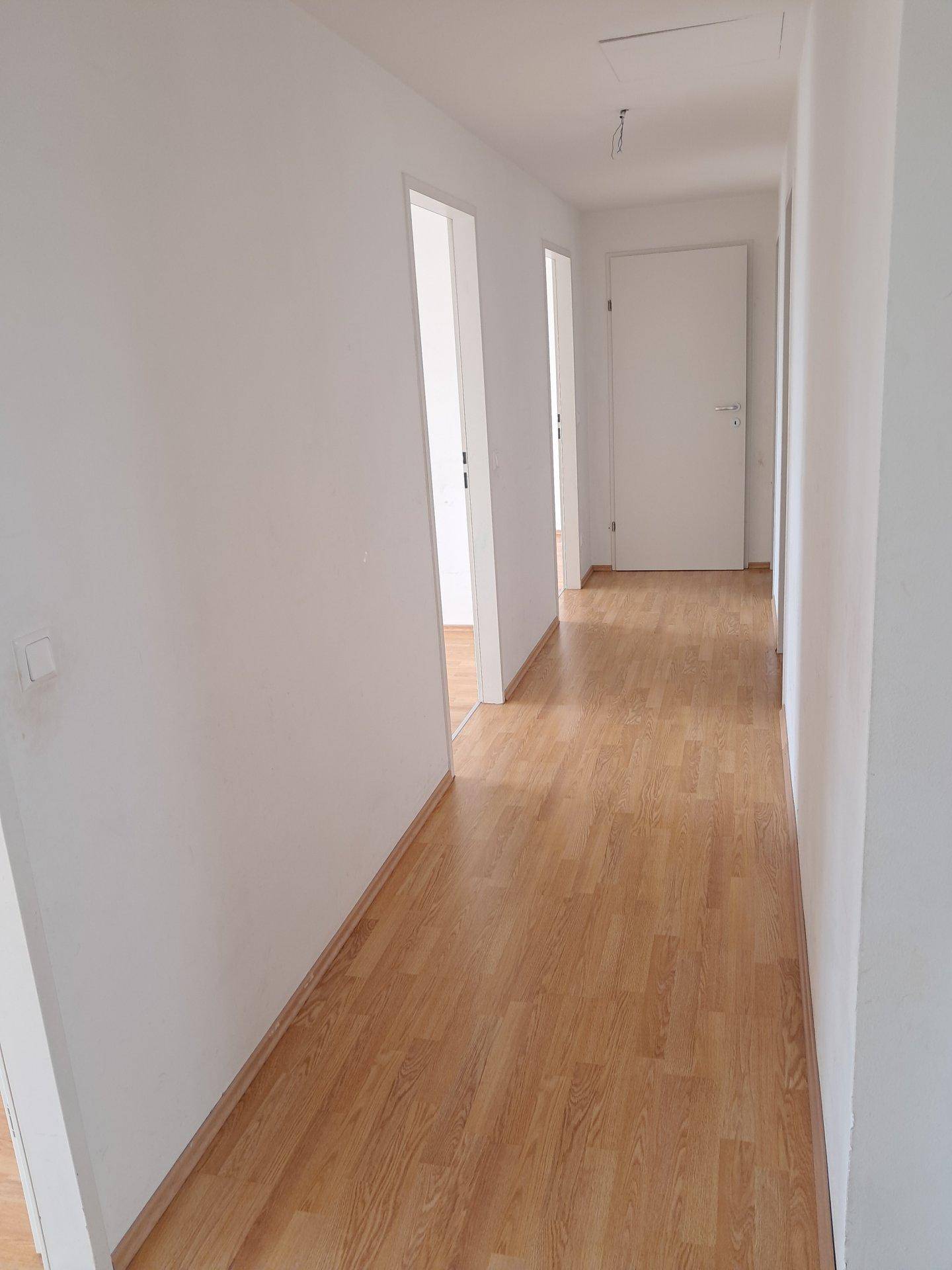 Heller Flur mit Laminatboden und weißen Wänden, der zu weiteren Räumen führt.