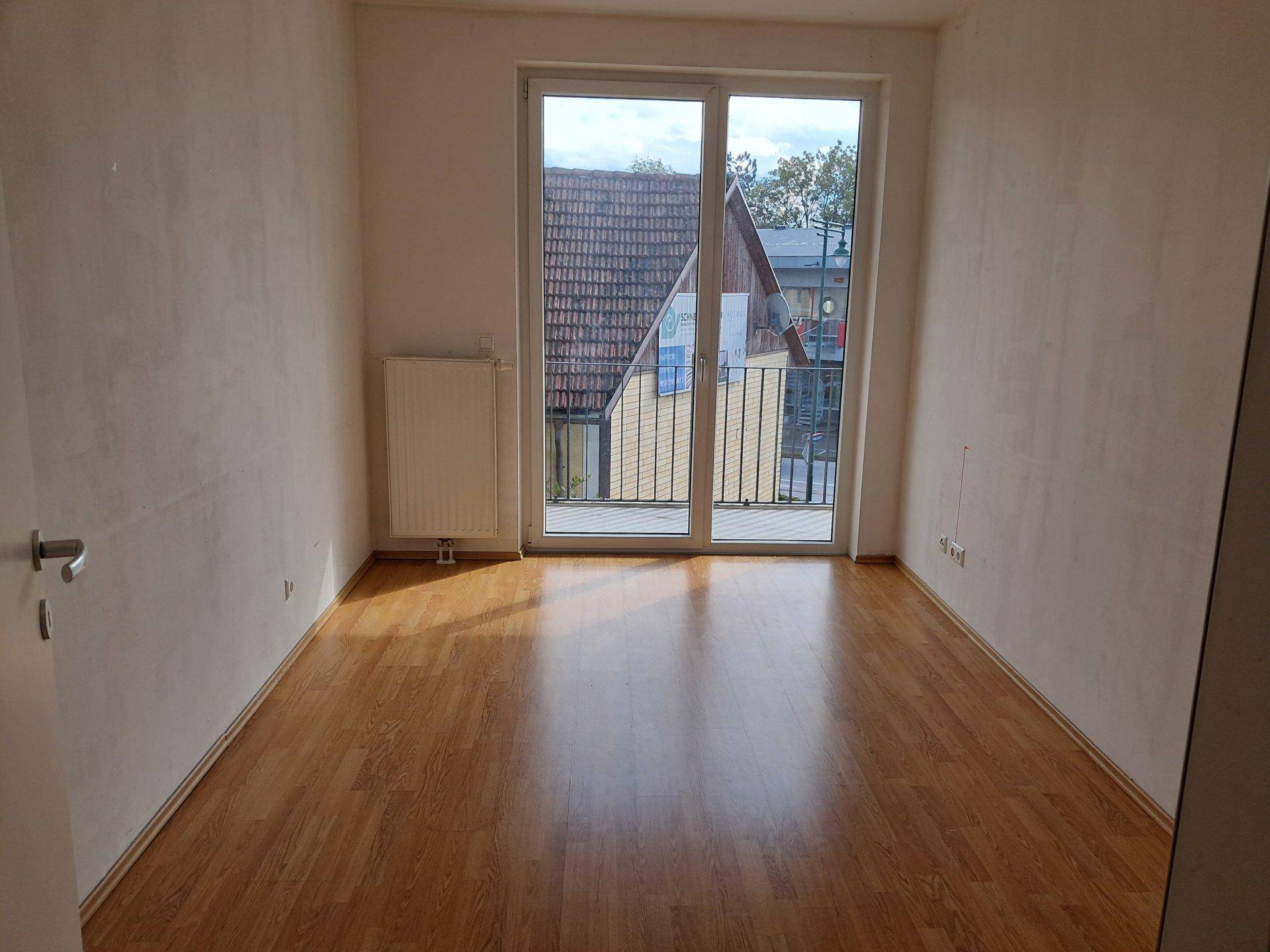 Leeres Schlafzimmer mit Laminatboden und Balkonzugang.