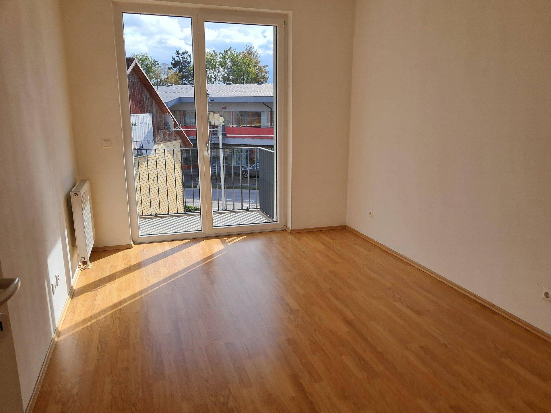 Helles Schlafzimmer mit Laminatboden und Zugang zu einem Balkon.