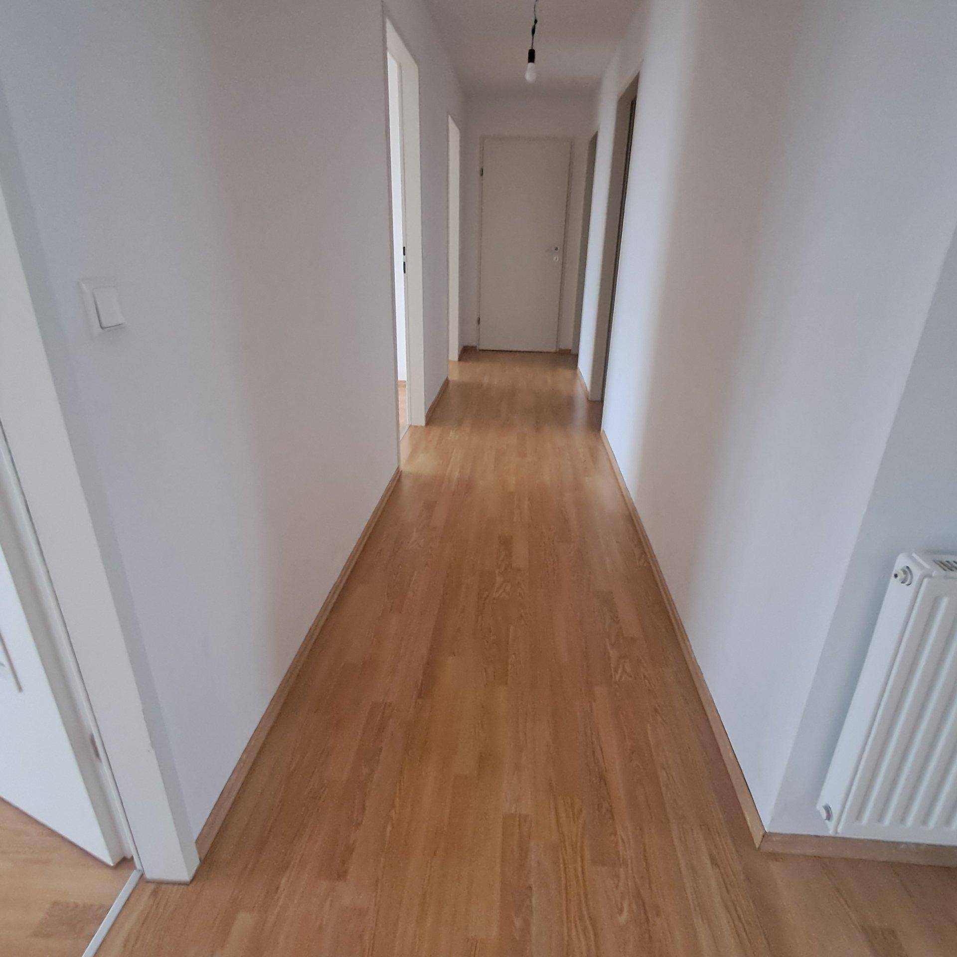 Heller Flur mit Laminatboden und weißen Wänden, der zu weiteren Räumen führt.