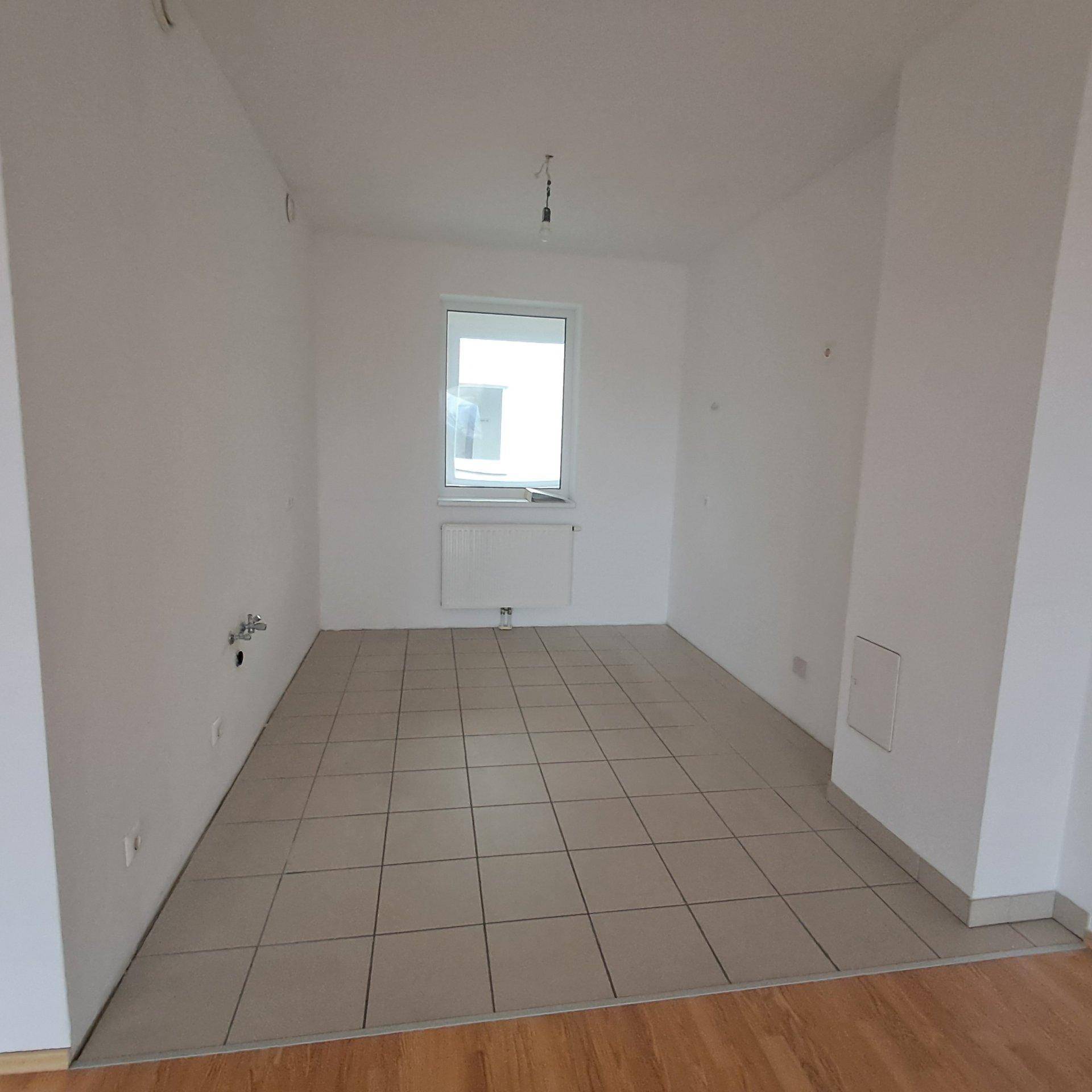 Leerer Raum mit hellen Fliesen und einem Fenster, bereit für die individuelle Einrichtung.