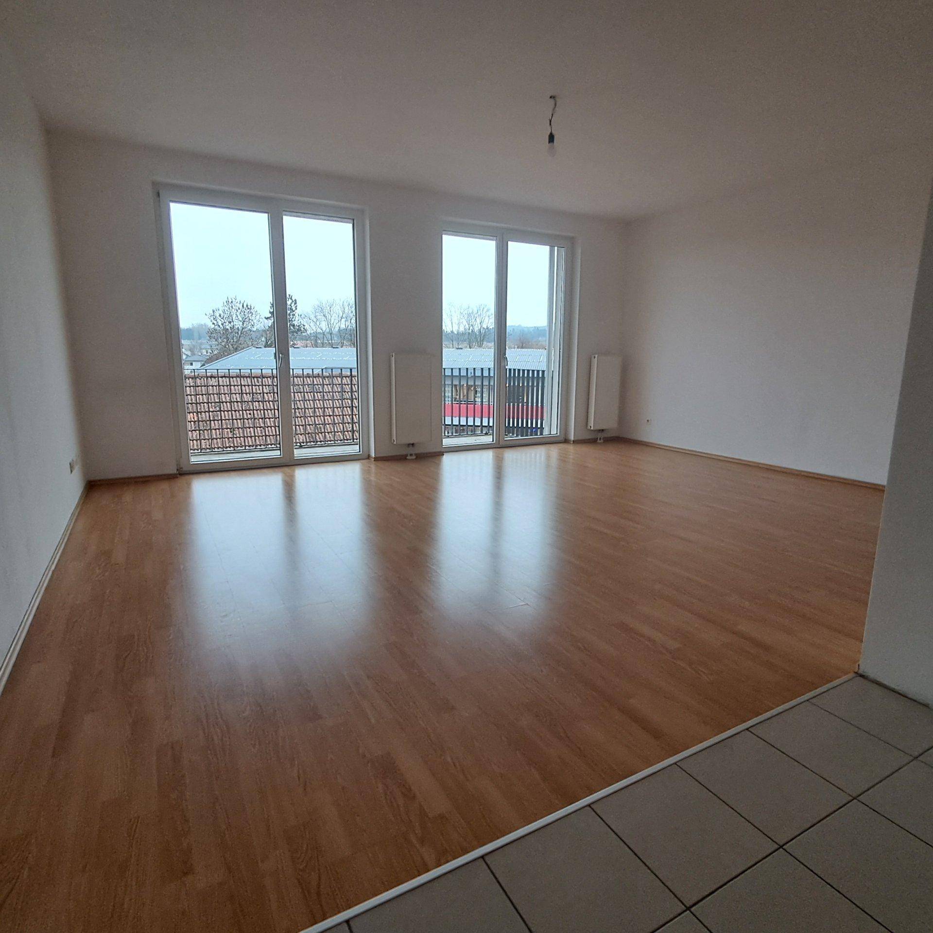 Helles Wohnzimmer mit Laminatboden und großen Fenstern, die viel Tageslicht hereinlassen.