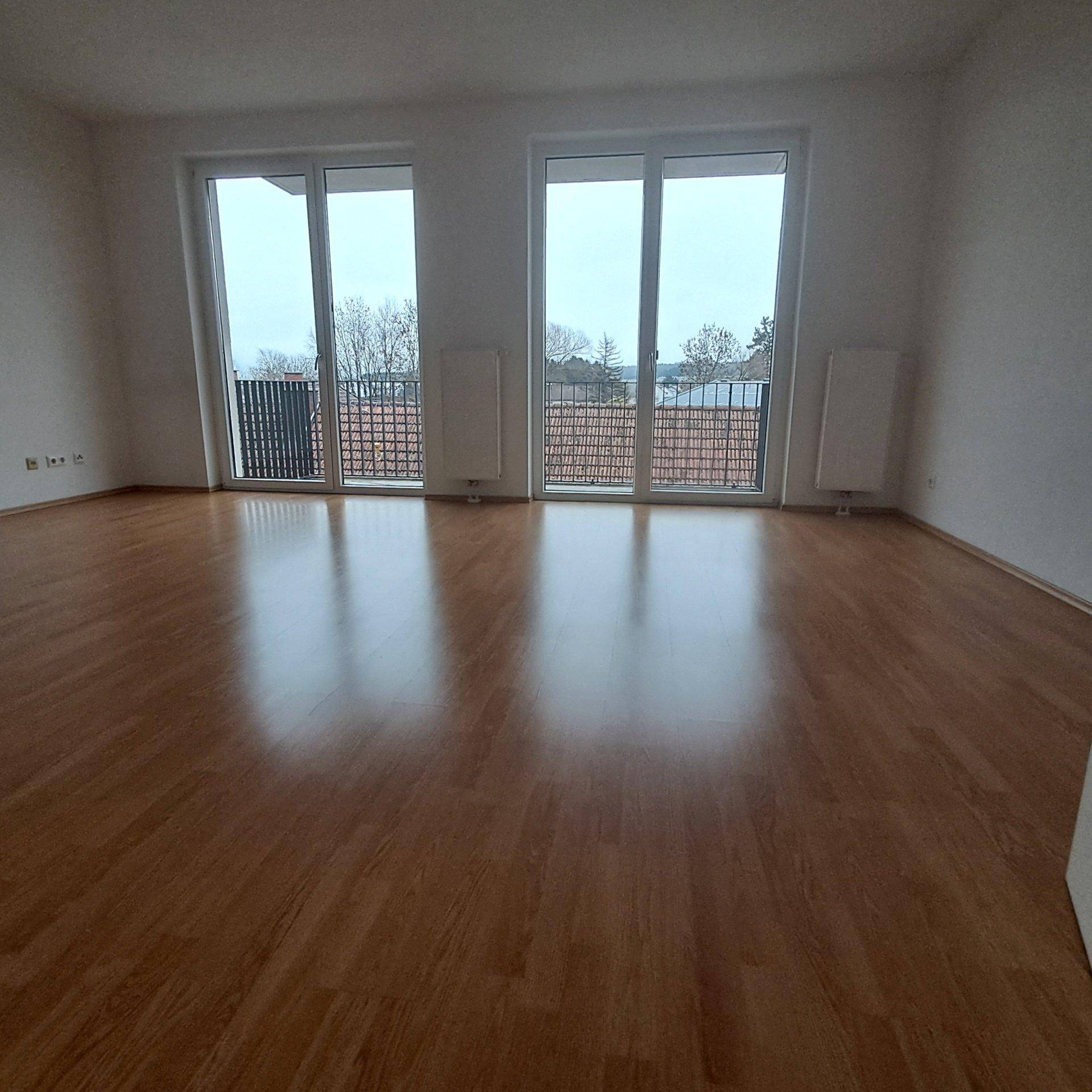 Geräumiges Wohnzimmer mit glänzendem Laminatboden und Zugang zu einem Balkon.