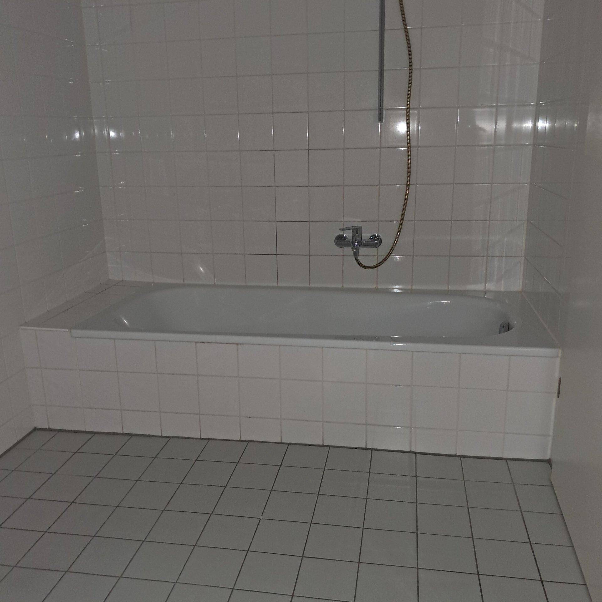Badezimmer mit weiß gefliester Badewanne und passenden Wand- und Bodenfliesen.