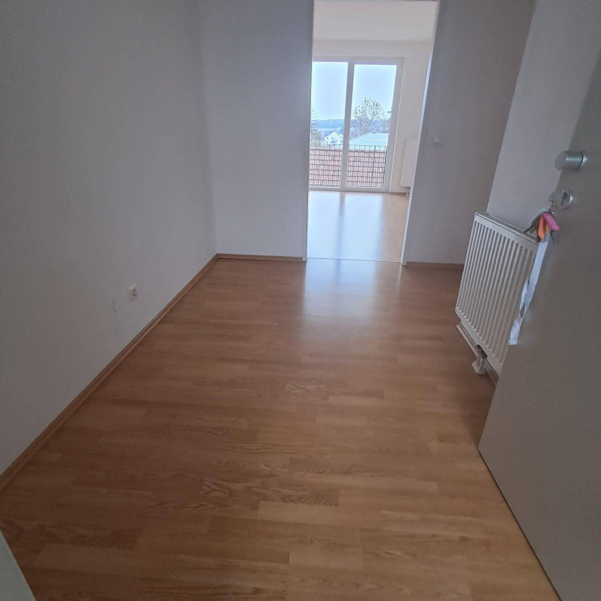 Zimmer mit Laminatboden und Blick in den angrenzenden Wohnbereich mit Balkonzugang.