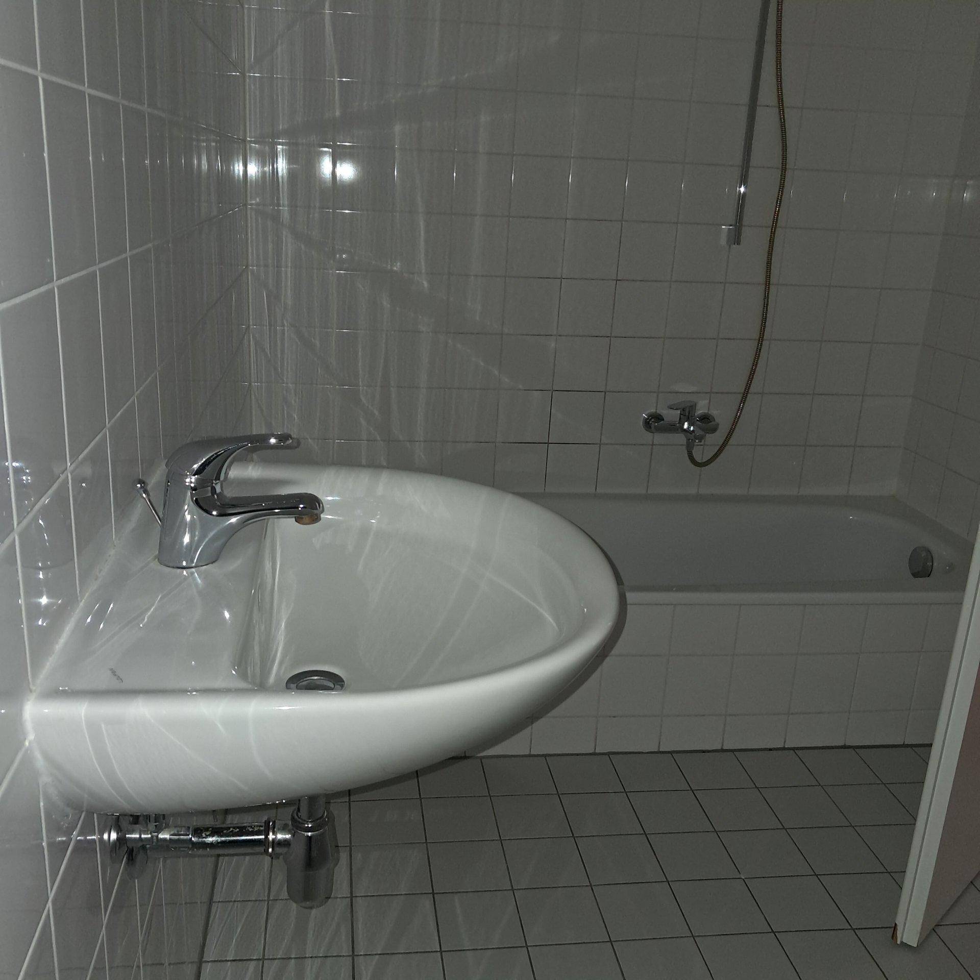 Funktionales Badezimmer mit Waschbecken, Badewanne und weißen Fliesen an Wänden und Boden.