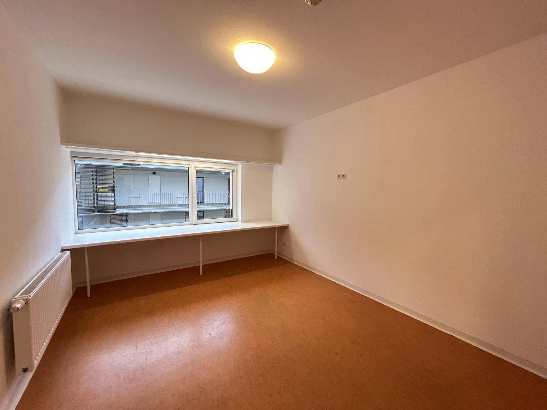 Leeres Zimmer mit großem Fenster, Vinylboden und Heizkörper, bereit zur Einrichtung.