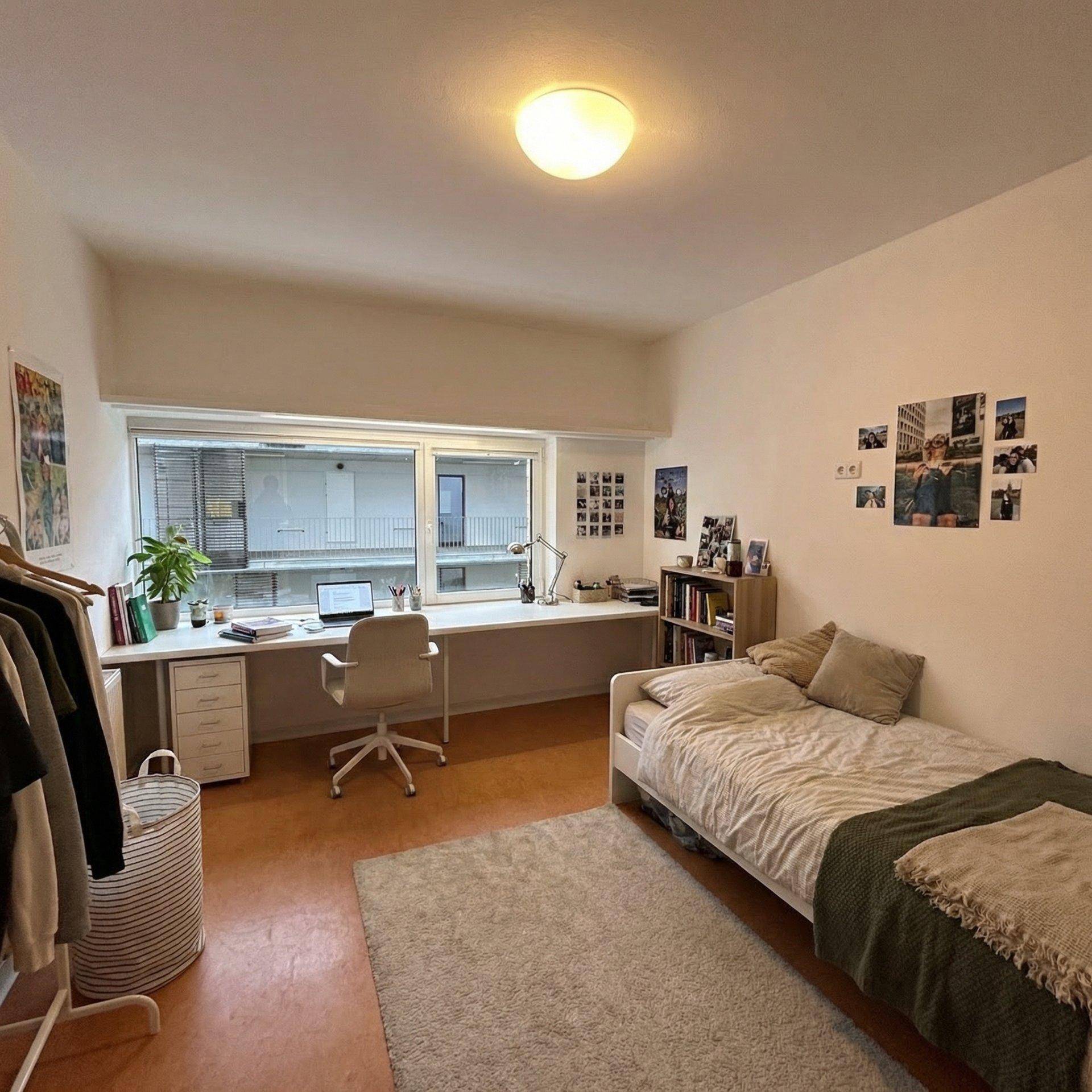 Helles Schlafzimmer mit Einzelbett, Schreibtisch und Fensterblick auf den Innenhof.