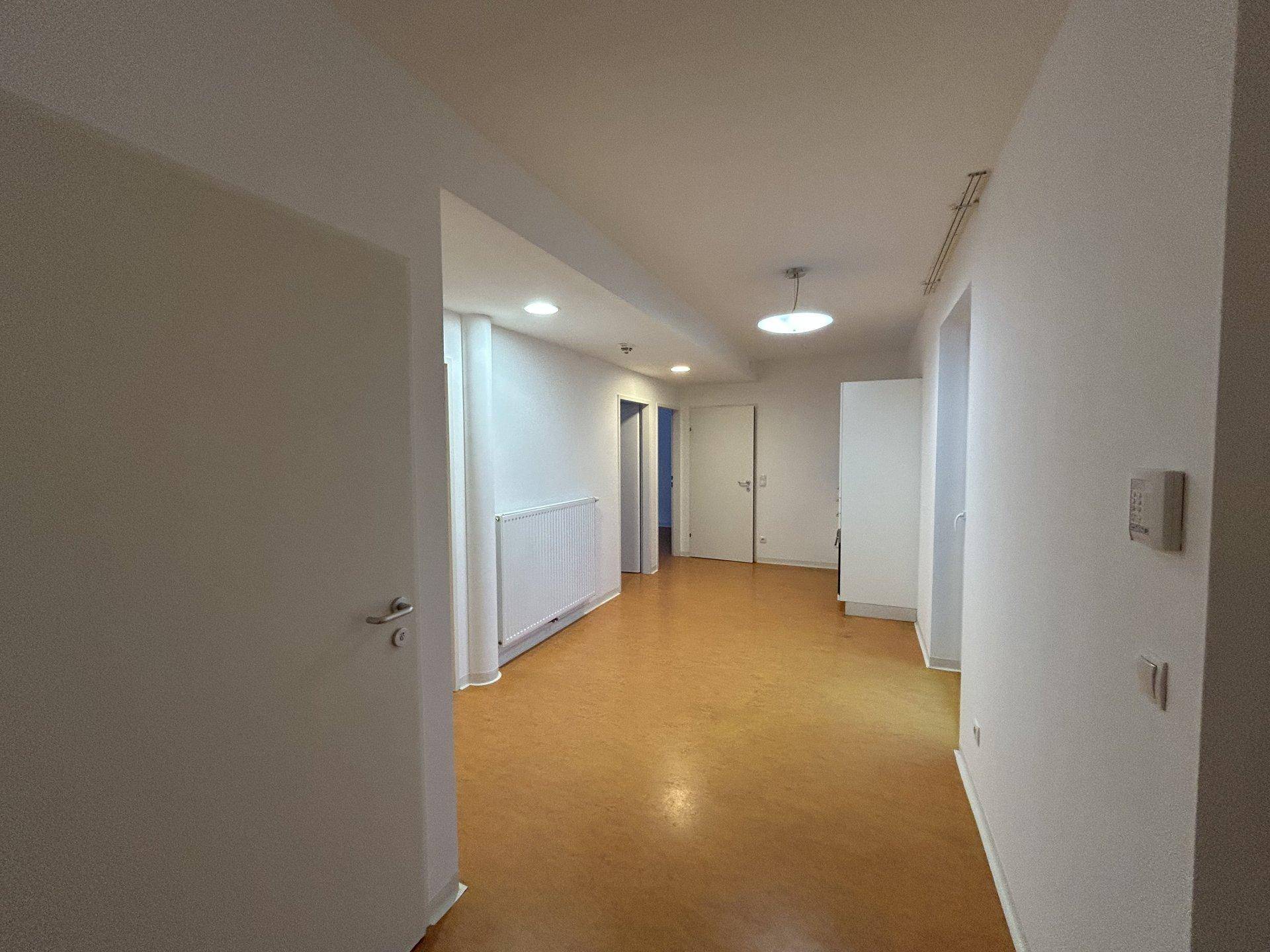 Heller Flur mit Vinylboden und weißen Wänden, der zu weiteren Räumen führt.