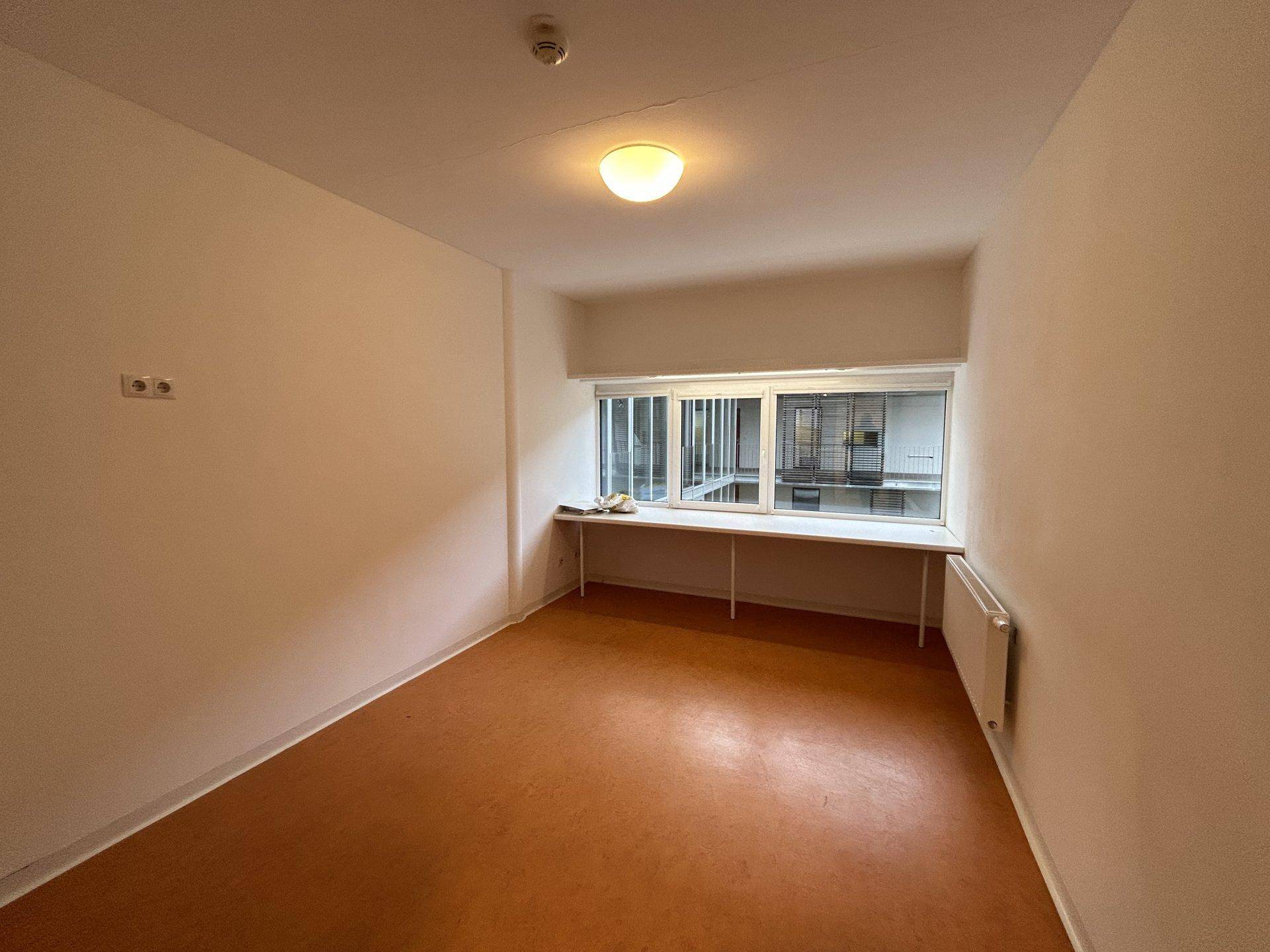 Geräumiges, leeres Zimmer mit breiter Fensterbank und Blick auf den Innenhof.