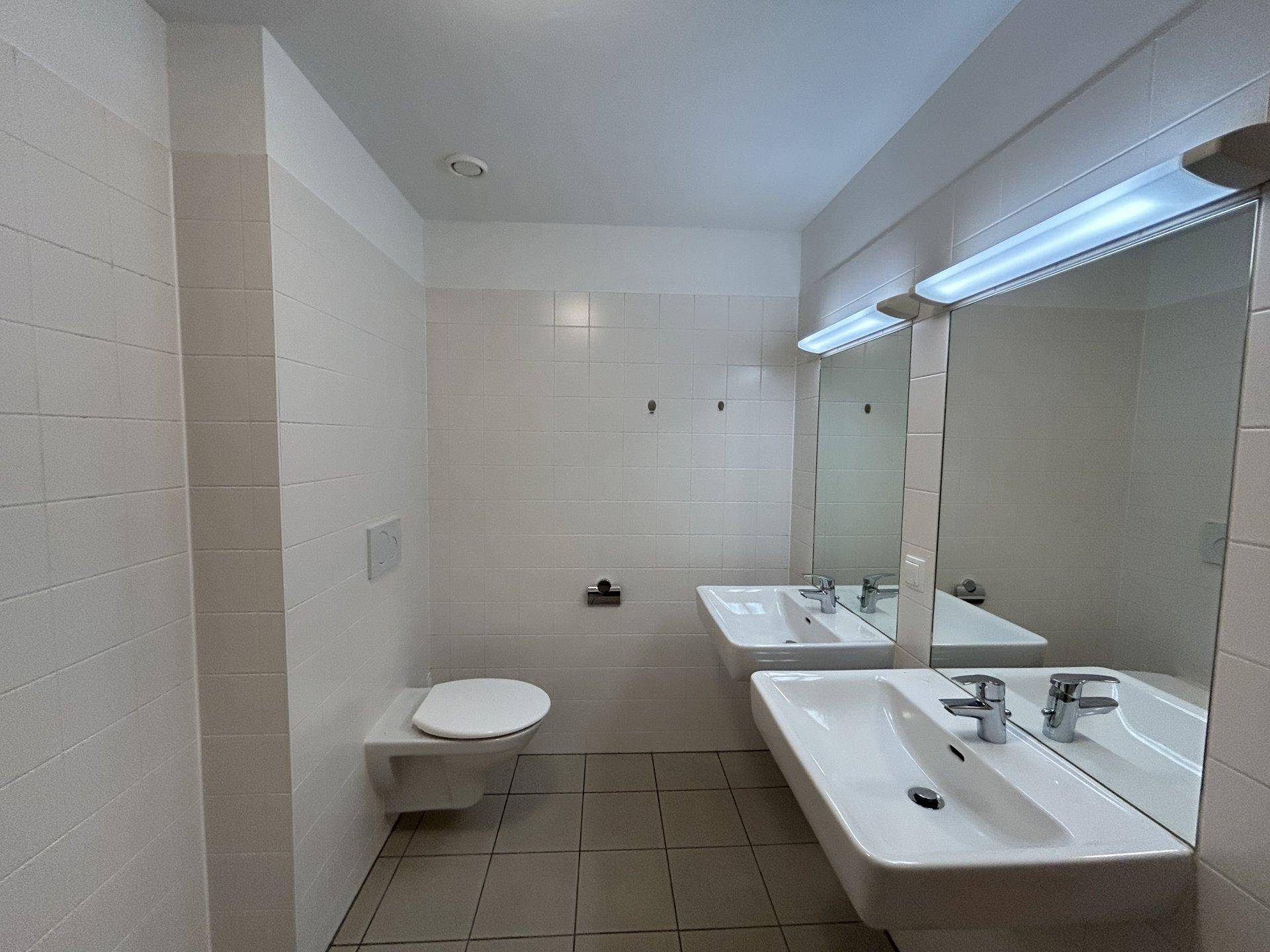 Modernes Badezimmer mit zwei Waschbecken, Wand-WC und großem Spiegel.
