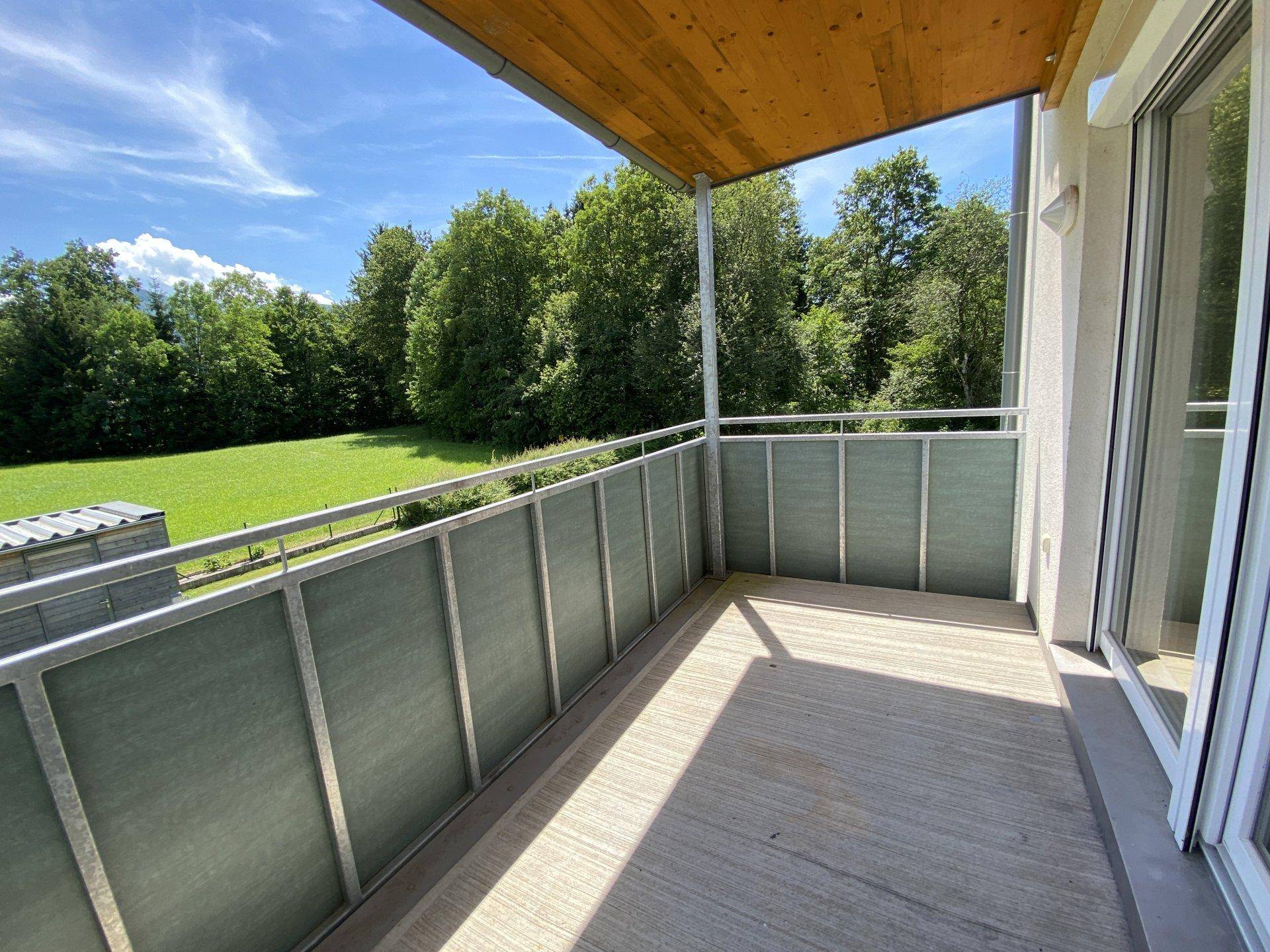 Überdachter Balkon mit Betonboden, Metallgeländer und Holzdecke, bietet einen schönen Blick ins Grüne.