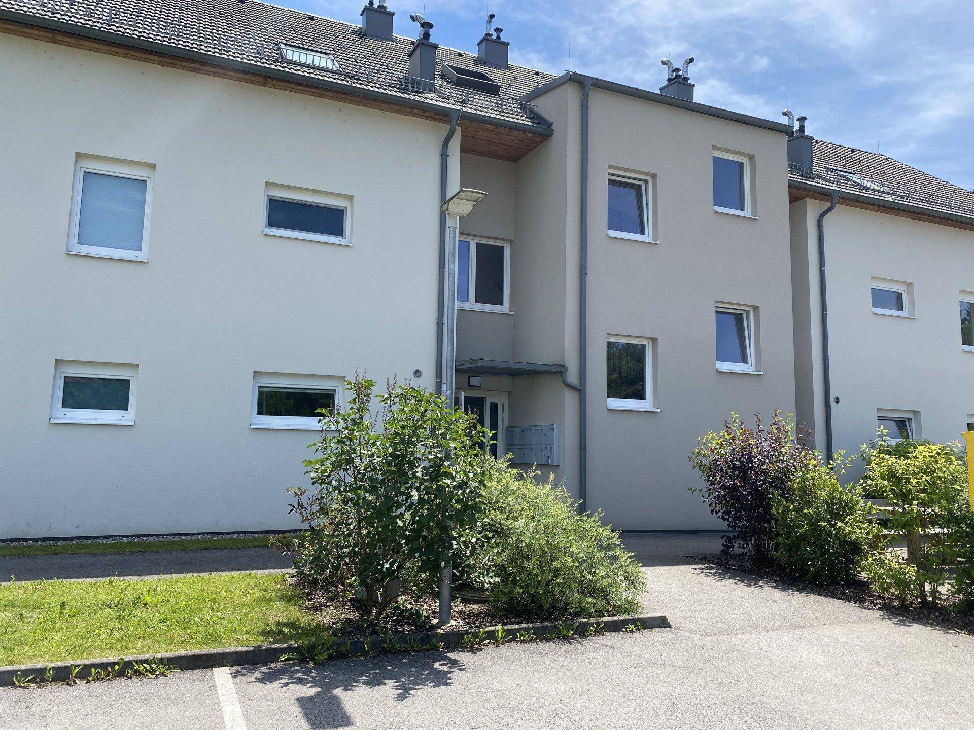 Vorderansicht des Wohngebäudes mit Eingangsbereich, Fenstern und gepflegten Grünflächen.
