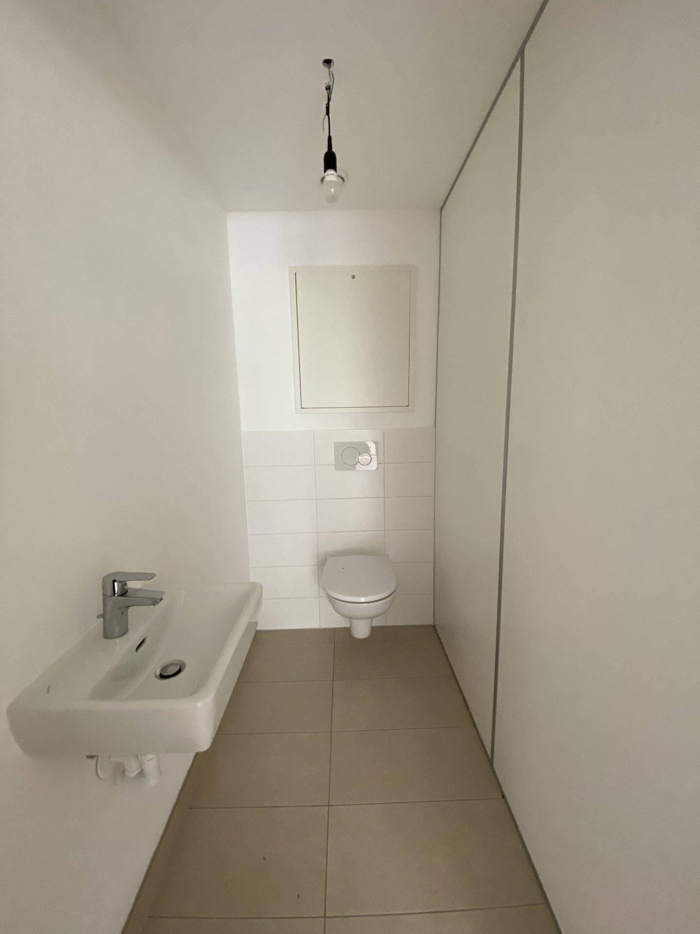 Modernes Gäste-WC mit wandhängender Toilette, kleinem Waschbecken und hellen Fliesen.