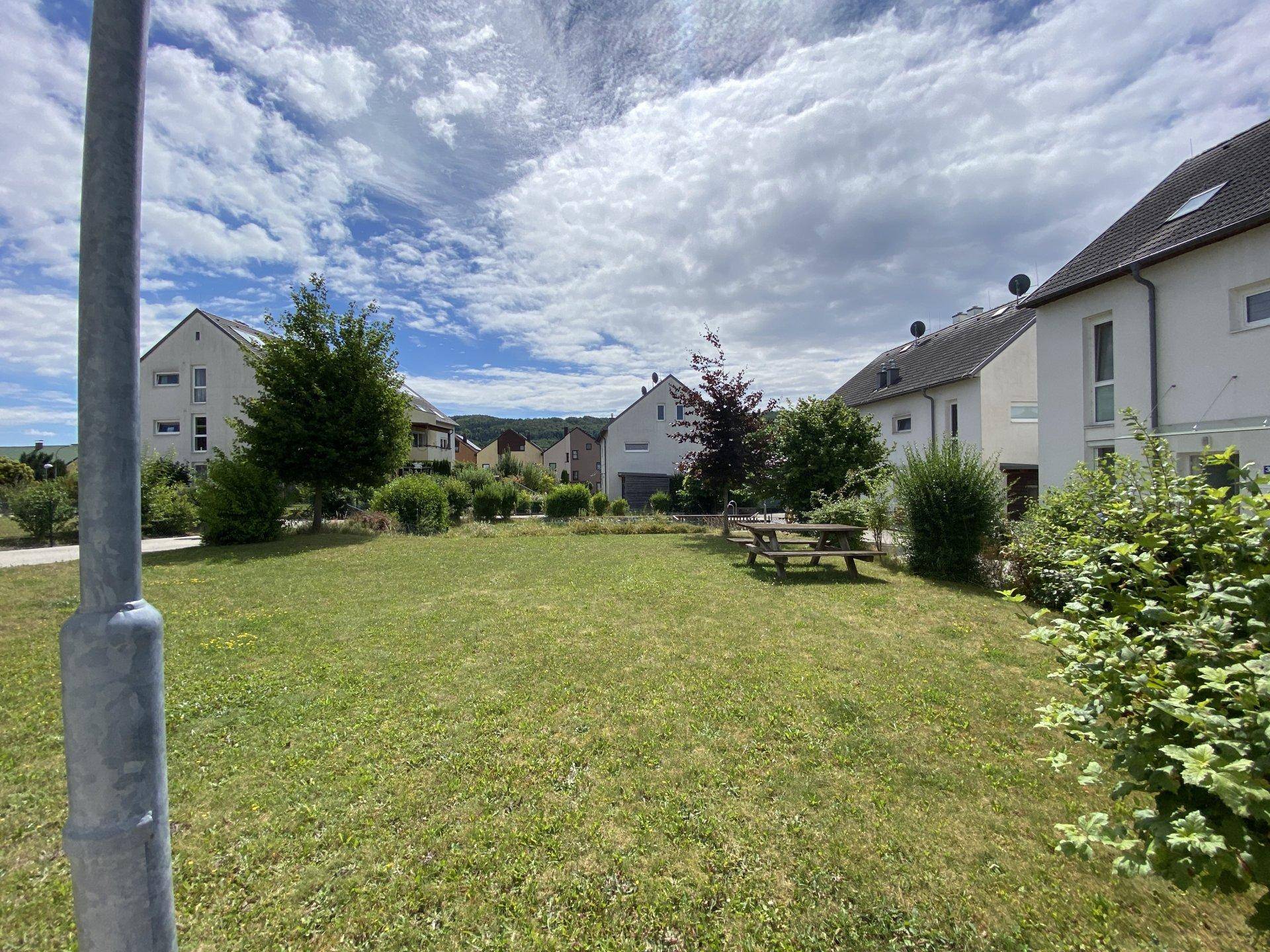 Große Grünfläche mit Picknicktisch und Wohngebäuden in ländlicher Umgebung unter weitem Himmel.