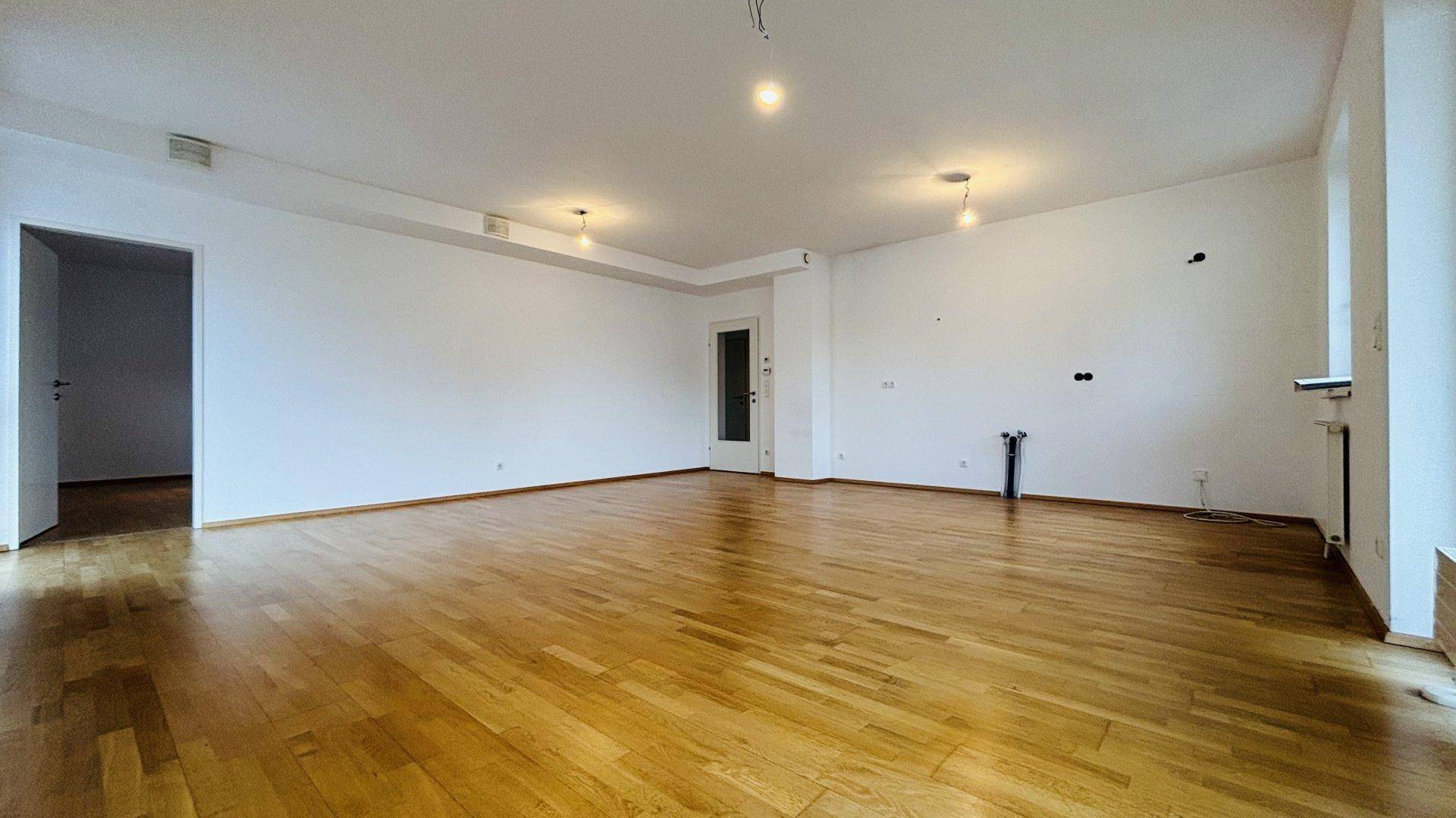 Geräumiges, leeres Wohnzimmer mit hellem Parkettboden und weißen Wänden, bereit zur individuellen Gestaltung.