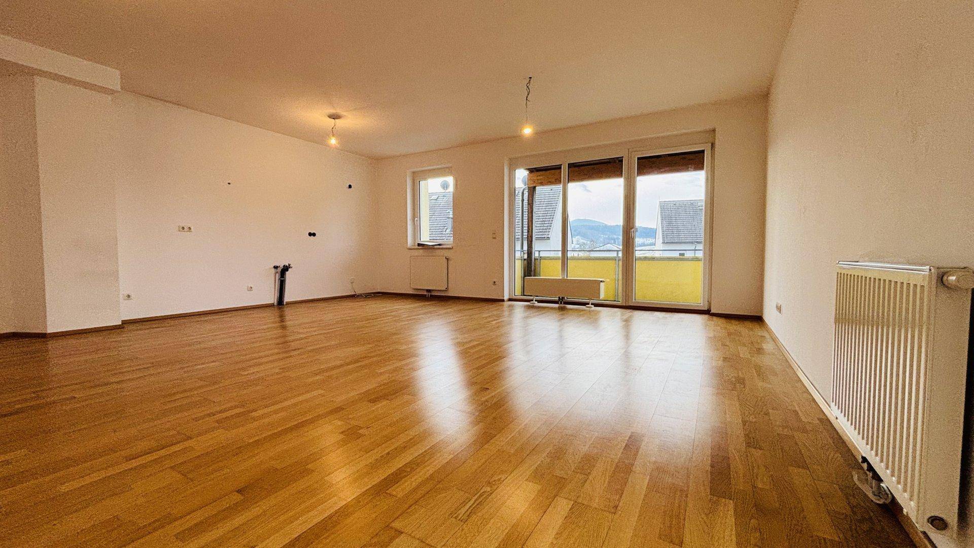 Helles Wohnzimmer mit Parkettboden und großzügigem Balkonzugang, bietet weite Aussicht auf die Umgebung.
