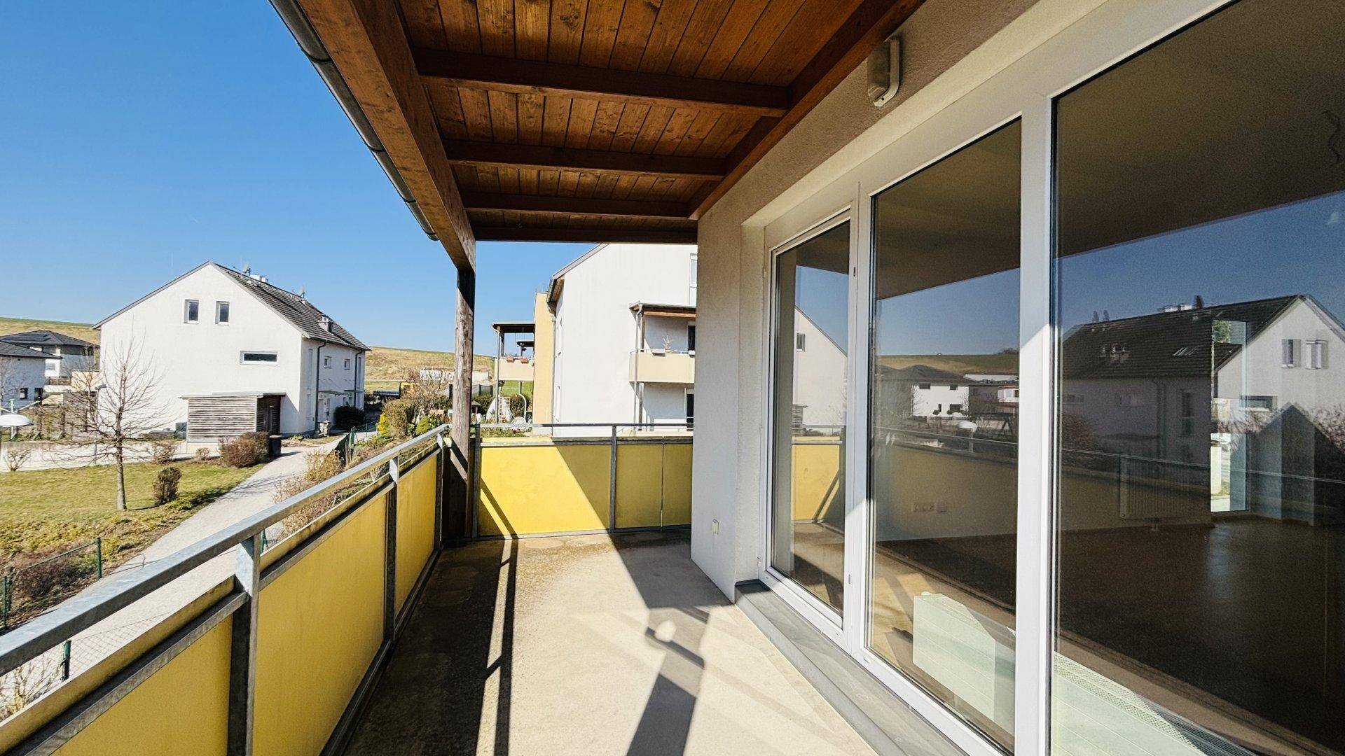Geräumiger Balkon mit großen Glasschiebetüren und Holzdach, bietet Zugang zum Innenbereich und Ausblick.