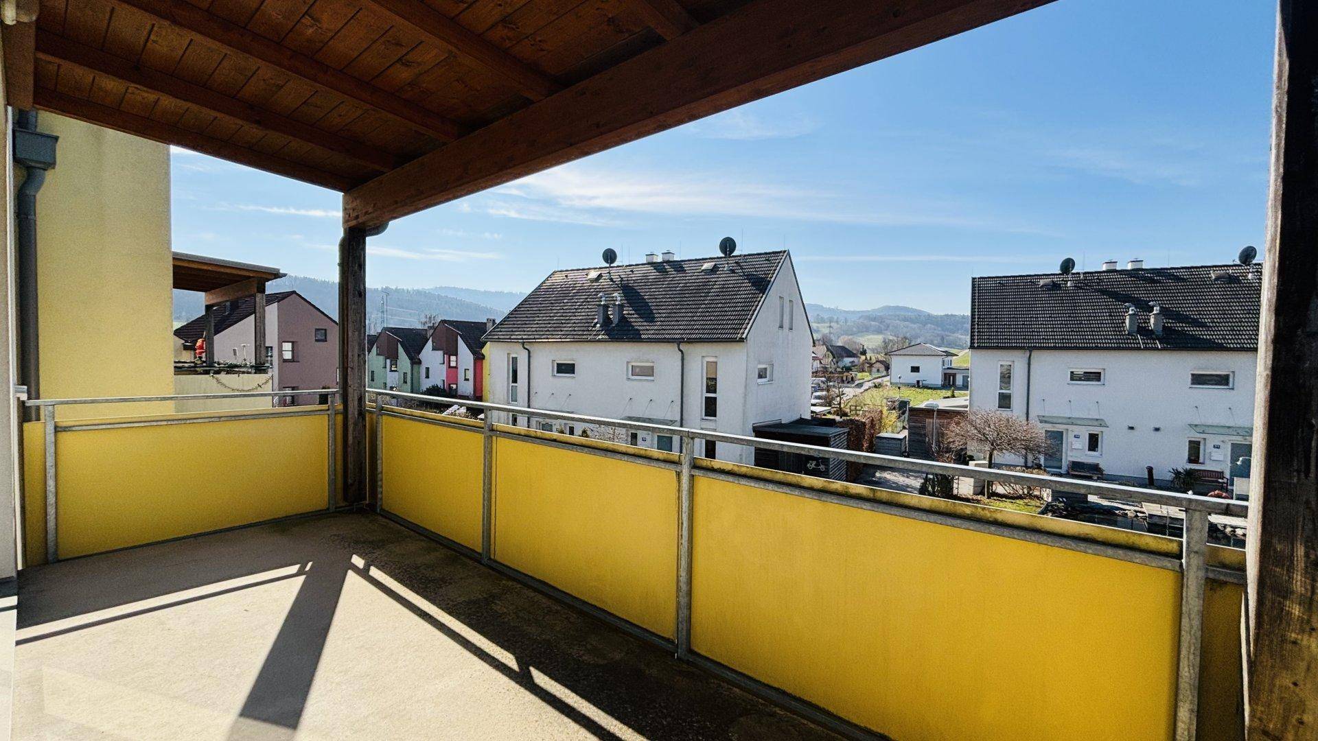 Überdachter Balkon mit Holzdach und gelber Brüstung, bietet einen schönen Blick auf die umliegende Landschaft.