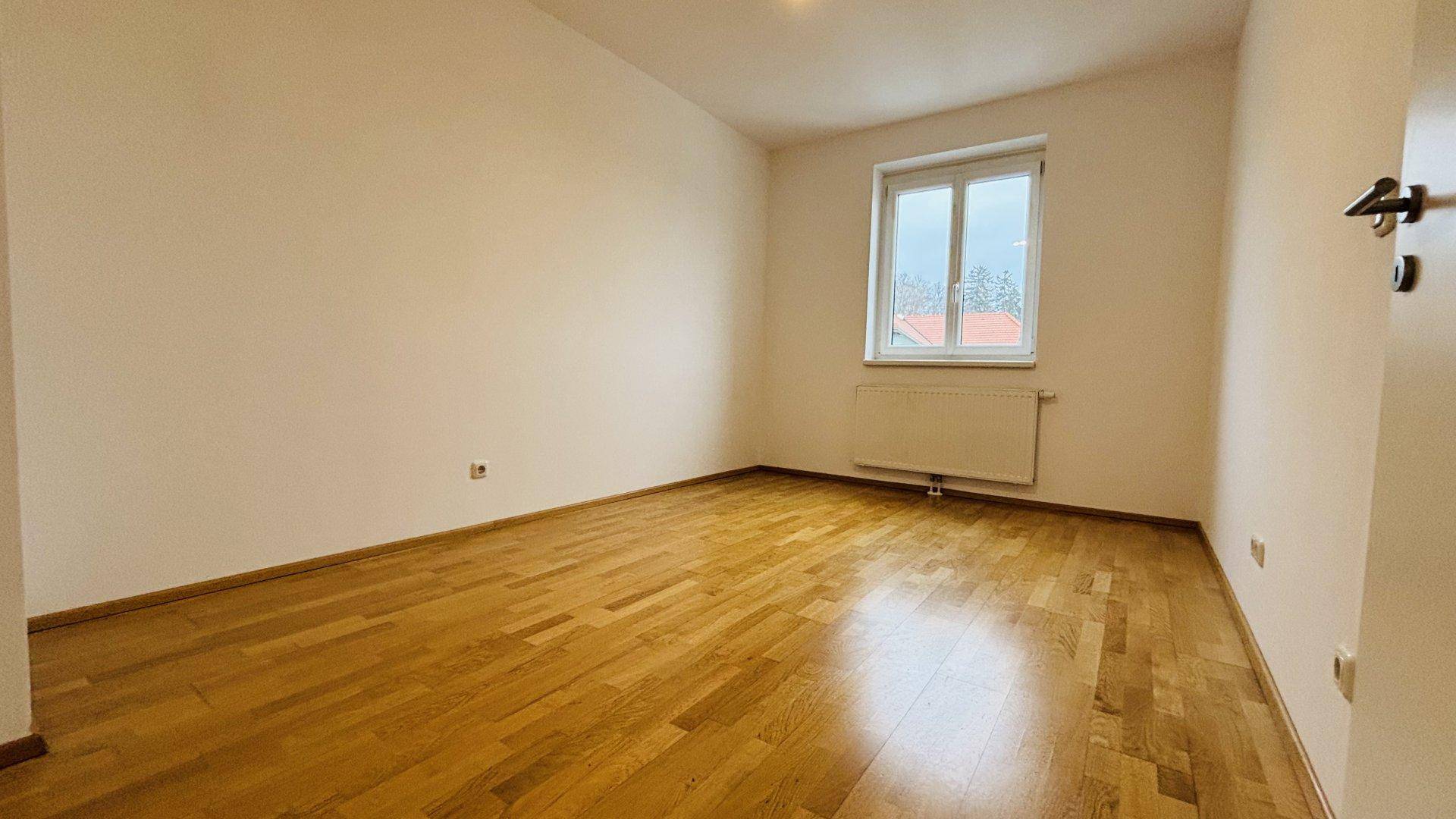 Gemütliches Schlafzimmer mit hellem Parkettboden und Fenster, ideal für erholsame Nächte.