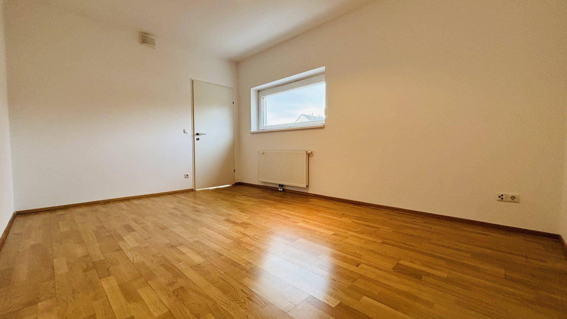 Helles Schlafzimmer mit Parkettboden und Fenster, bietet eine ruhige und gemütliche Atmosphäre.