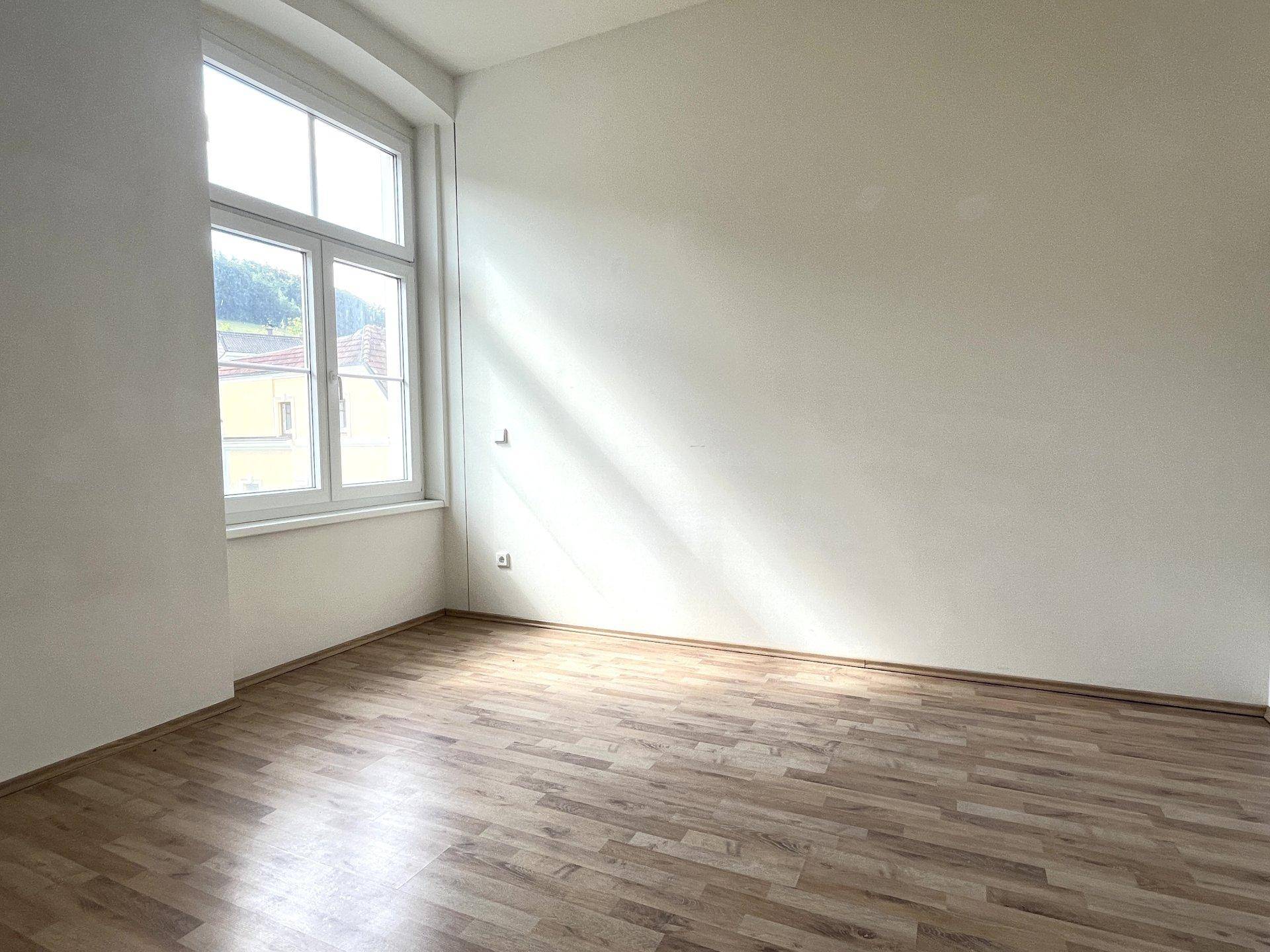 Lichtdurchfluteter Raum mit Laminatboden und einem großen Fenster, das den Blick nach draußen freigibt.