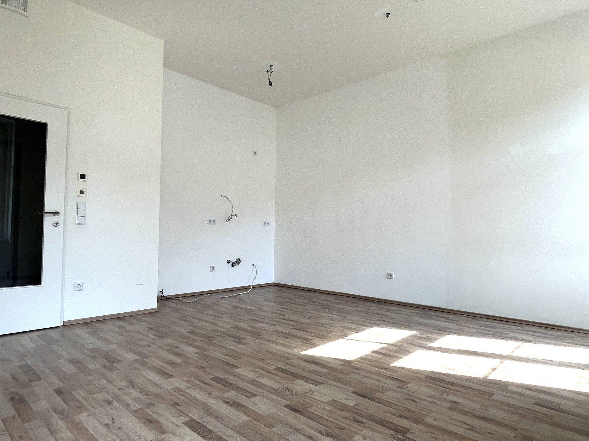 Geräumiger, heller Raum mit Laminatboden und einer Tür, bereit für die individuelle Einrichtung.