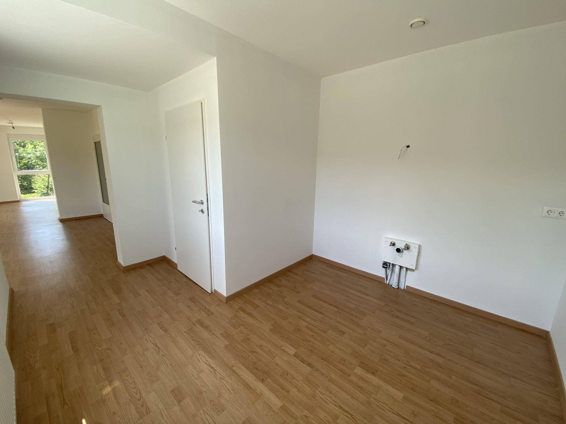 Leerer Raum mit Holzboden und Anschlüssen für eine Küche, bereit für die Installation.