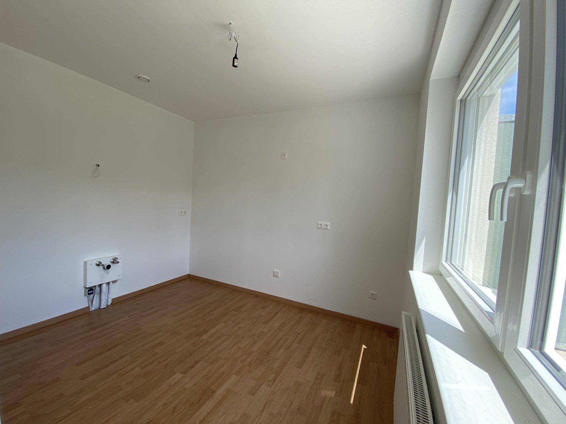 Unmöblierter Küchenbereich mit Holzboden, Fenster und Heizkörper, bereit für die Einrichtung.