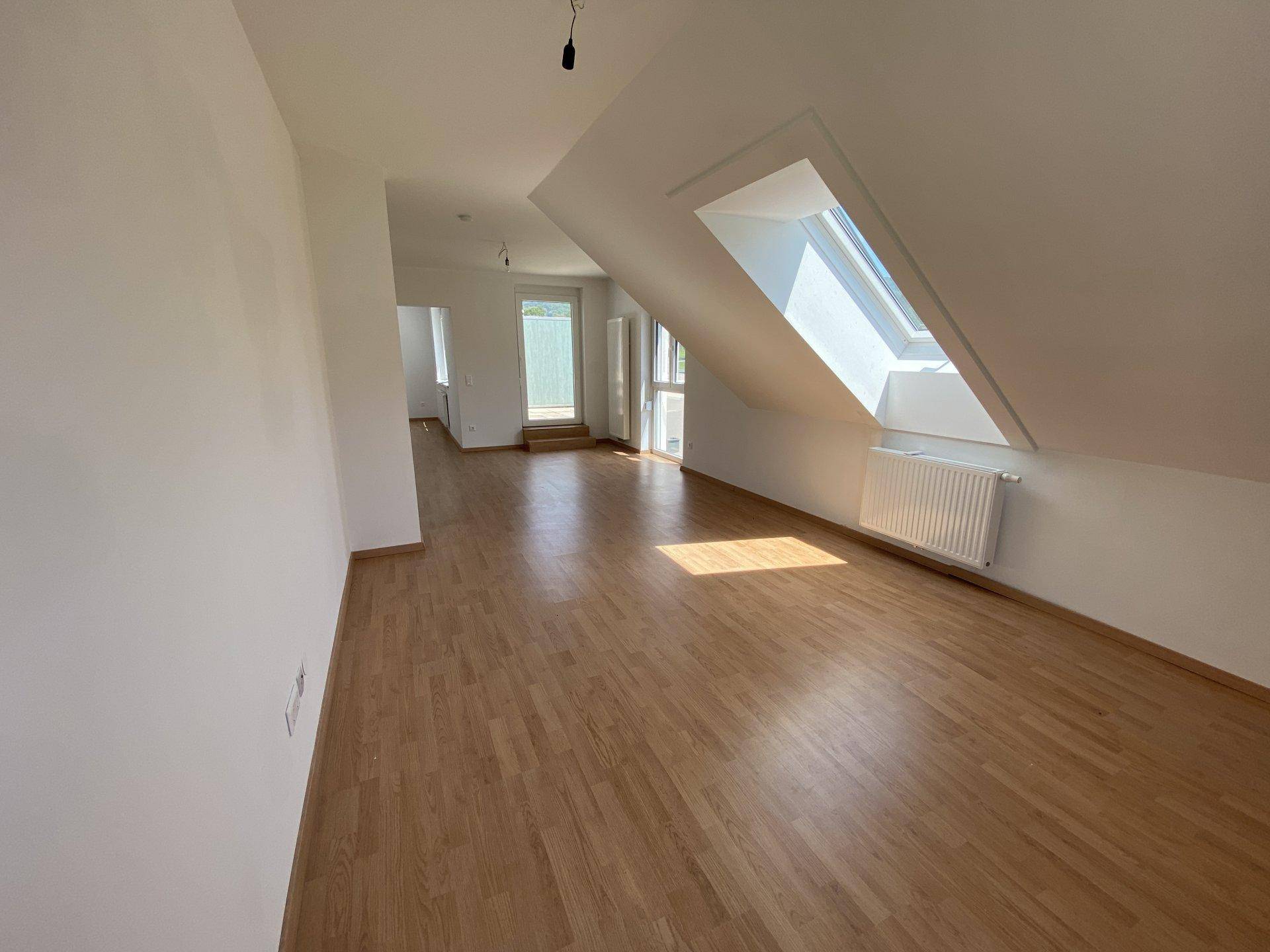 Heller Wohnbereich mit Holzboden, Dachschräge und einem großen Dachfenster, das den Raum erhellt.