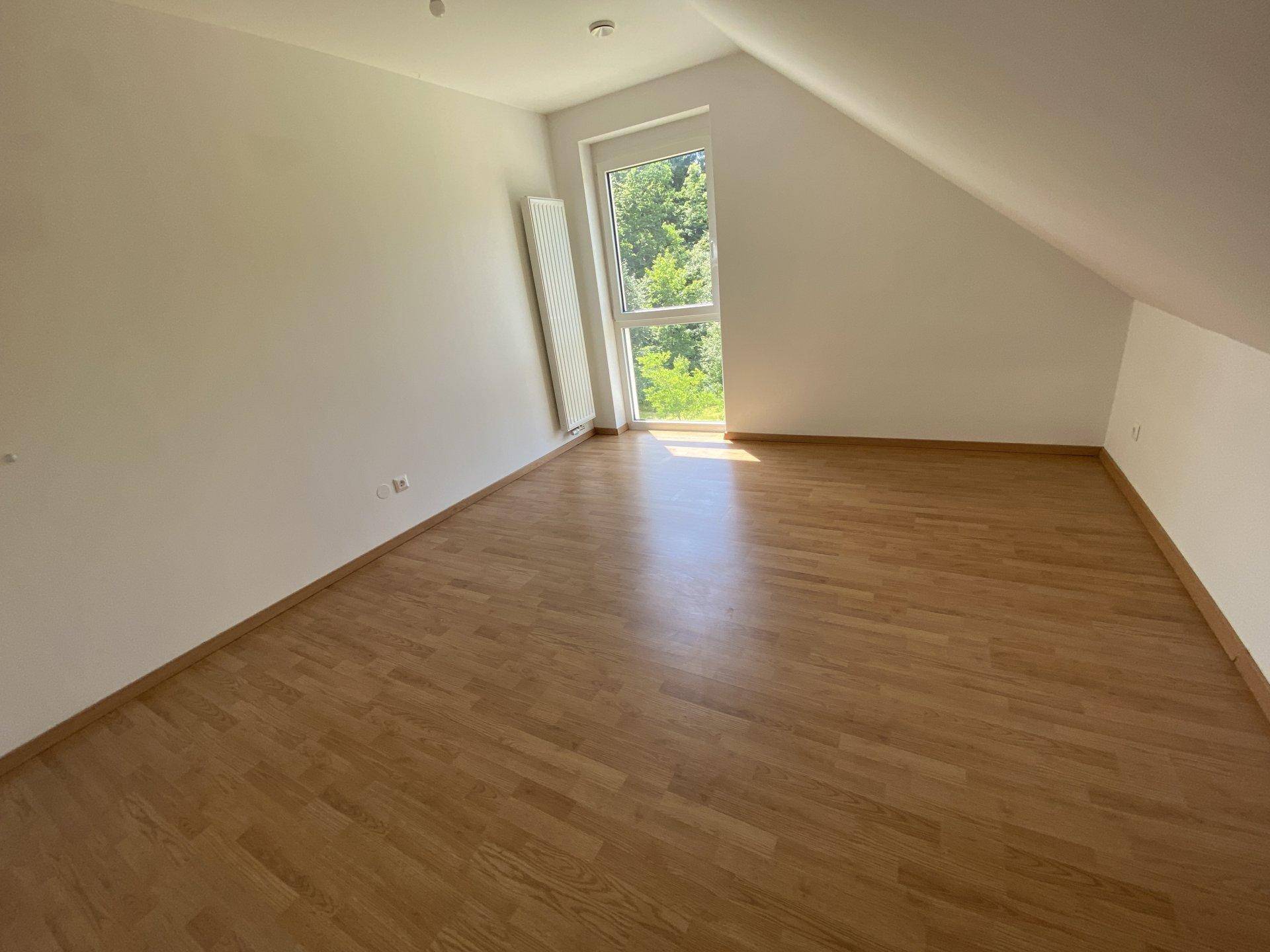 Leeres Schlafzimmer mit Holzboden, großem Fenster und Dachschräge, bietet viel Gestaltungspotenzial.