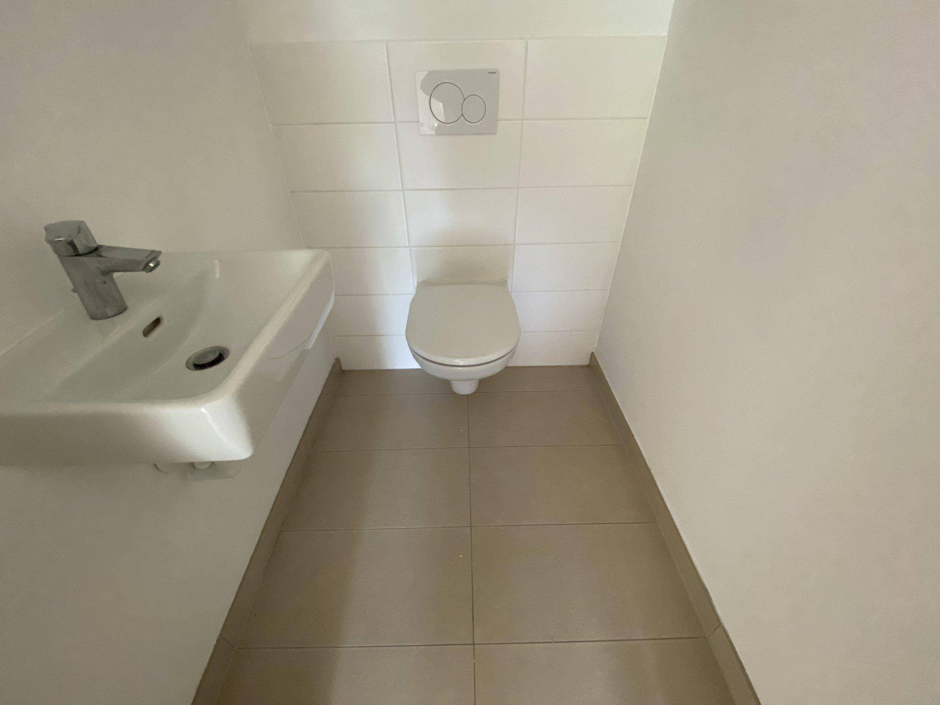 Modernes Gäste-WC mit wandhängender Toilette und kleinem Waschbecken, hell gefliest.