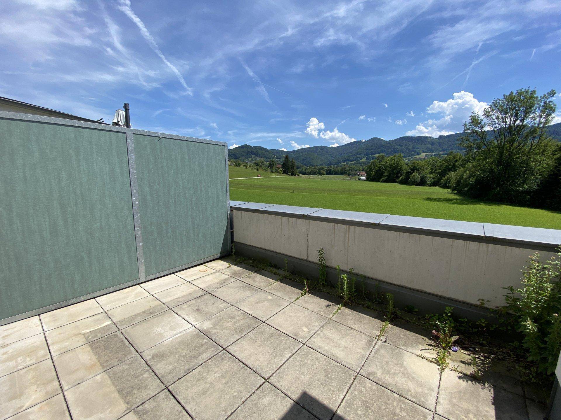 Geräumige, unmöblierte Terrasse mit Fliesenboden und weitem Blick auf die grüne Landschaft.