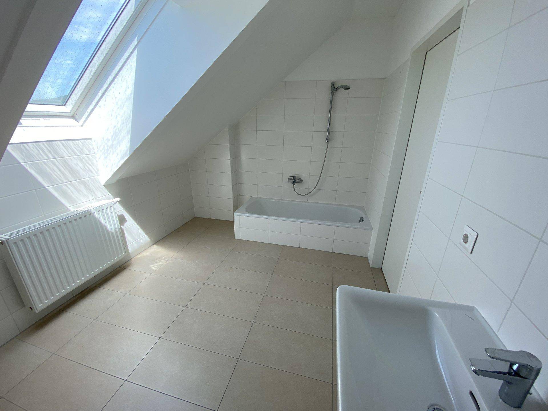 Helles Badezimmer mit Badewanne, Fliesenboden und Dachfenster, das viel Tageslicht spendet.