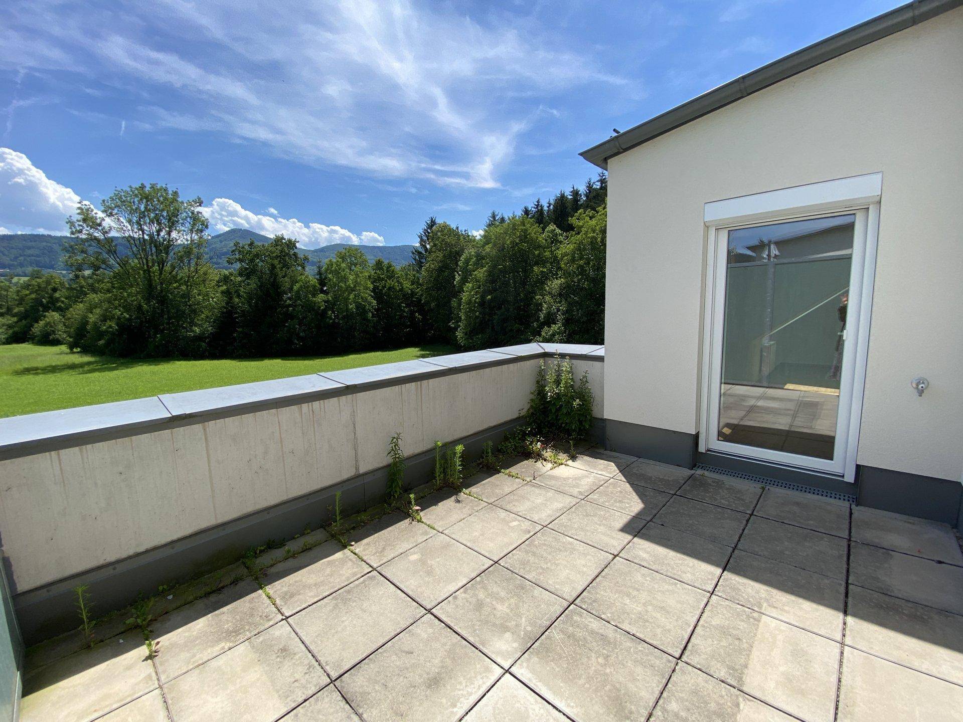 Leere Terrasse mit Fliesenboden und Zugangstür, bietet einen schönen Blick ins Grüne.